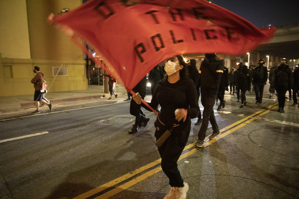 Protestors, clad in all black, crossed the 10 freeway on S Grand Ave, led by a demonstrator holding a "Defund the police" flag.