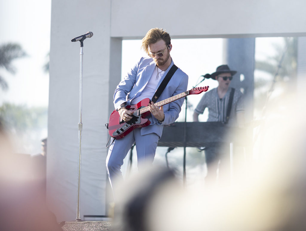 Donning an unbuttoned blue suit over a plain white top, FINNEAS plays his red electric guitar. The artist frequently played both guitar and piano while serenading the audience. (Ashley Kenney/Photo editor)