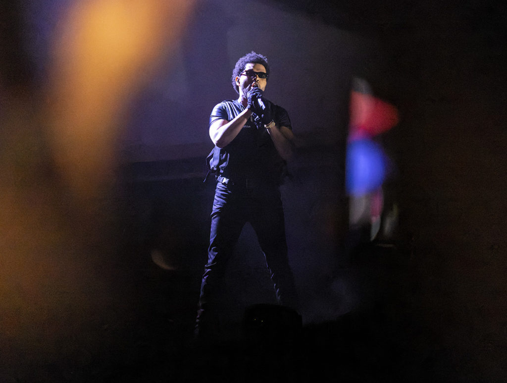 Wearing all black, The Weeknd grasps a microphone on stage. The performer was the final headliner for the last day of Coachella 2022, singing tracks from across his discography. (Ashley Kenney/Photo editor)