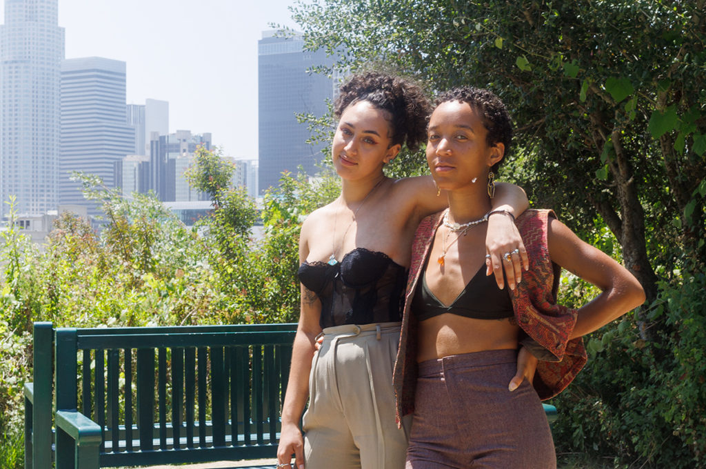 The duo stand with arms around one another in front of greenery and an urban backdrop. Zeinah said her music, particularly the acoustic guitar composition, is inspired by the grainer vocals of musician Summer Walker. (Finn Chitwood/Daily Bruin)