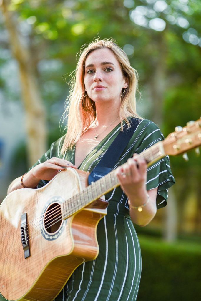 Wood stands in a green dress and holds her guitar. Inspired by the ocean and human sentimentality, "flowers and champagne" explores the singer&squot;s more stripped-down, folk capabilities. (Ariana Fadel/Daily Bruin staff)