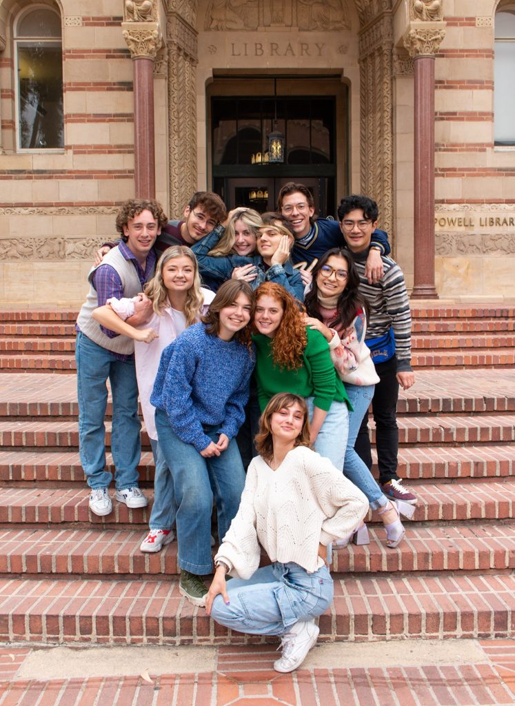 Members of Company cluster around one another on the steps of Powell Library. The group's prerecorded skits feature locations such as Barney's Beanery, Janss Steps and a dorm bathroom. (Megan Cai/Daily Bruin)