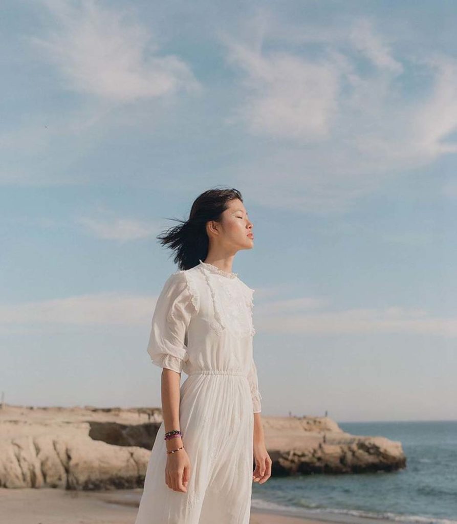 A figure in a white dress stands angled into the wind on a beach. Yang said their portraits used to be more orchestrated, similar to an editorial style, but now they try to shoot subjects in an environment where they could usually be found. (Courtesy of Sey Yang)