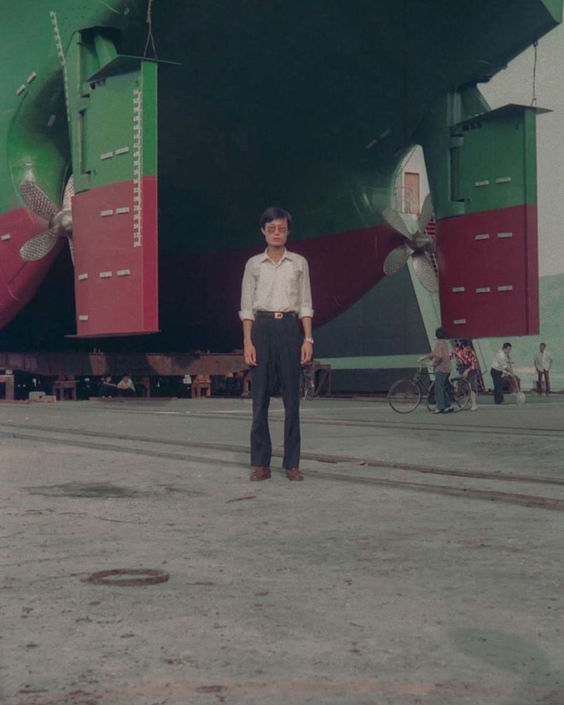 A man stands in front of a large green and red structure behind him. The photo is part of Yang&squot;s collection "I stop somewhere, waiting for you.," composed of their father&squot;s negatives from the 1990s which Yang color corrected and restored. (Courtesy of Sey Yang)