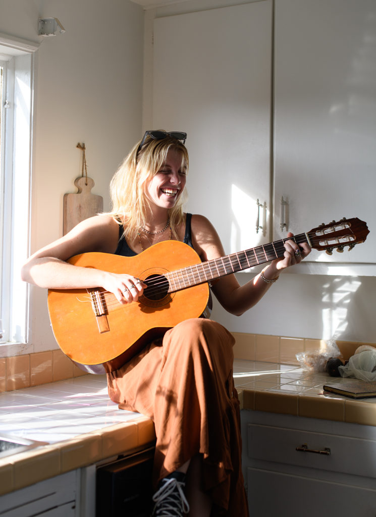 Bacino sits atop a kitchen counter strumming her guitar. Performing as Sophia Bacino & Friends, Bacino and her bandmates will blend folk and indie pop on the Spring Sing stage. (Sakshi Joglekar/Assistant Photo editor)