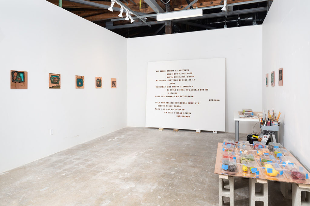 A large gypsum board with letters composed of soil stands against the back wall of a studio space. For her thesis project, Amézquita said she formed letters from soil to honor and spell out the names of migrants who died in detention centers. (Courtesy of Jackie Amezquita)