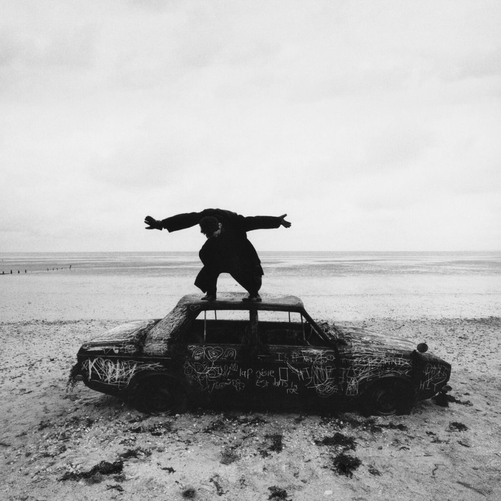 A man dressed in black stands on a car in a barren landscape on the cover of the 1975&squot;s "Being Funny in a Foreign Language." The indie-rock bands fifth album will debut Oct. 14.(Courtesy of Dirty Hit)