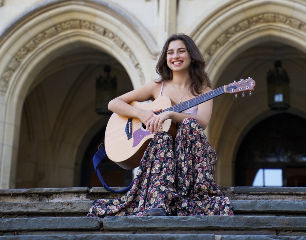 Dry sits on steps and holds her guitar on her lap. The singer-songwriter said they have found joy in developing folk style works. (Halinda Yu/Daily Bruin)
