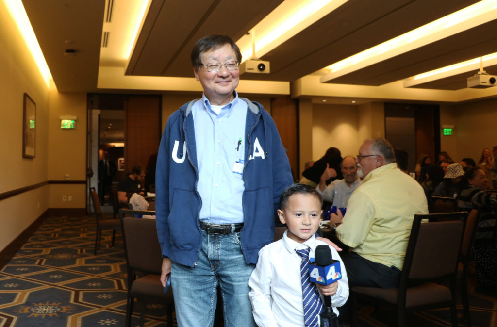 Wesley Rae (right) and Kaz Ando (left) stand smiling as Rae holds a microphone. Ando, one of the blood donors who helped save Rae's life, has been a regular donor for the past 20 years. (Courtesy of Noah Danesh)