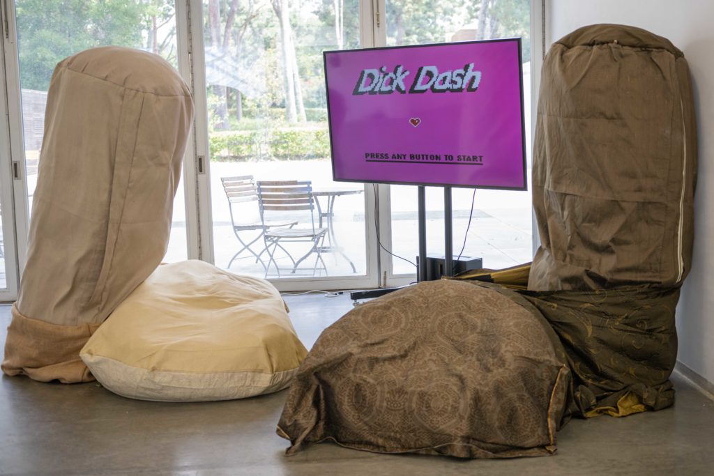 Surrounded by genitalia-shaped furniture, a television displays the electric pink start screen for Joy Yang&squot;s "Dick Dash." The fourth-year said the 2D platformer can be played using breast-shaped controllers. (Brandon Morquecho/Assistant Photo editor)