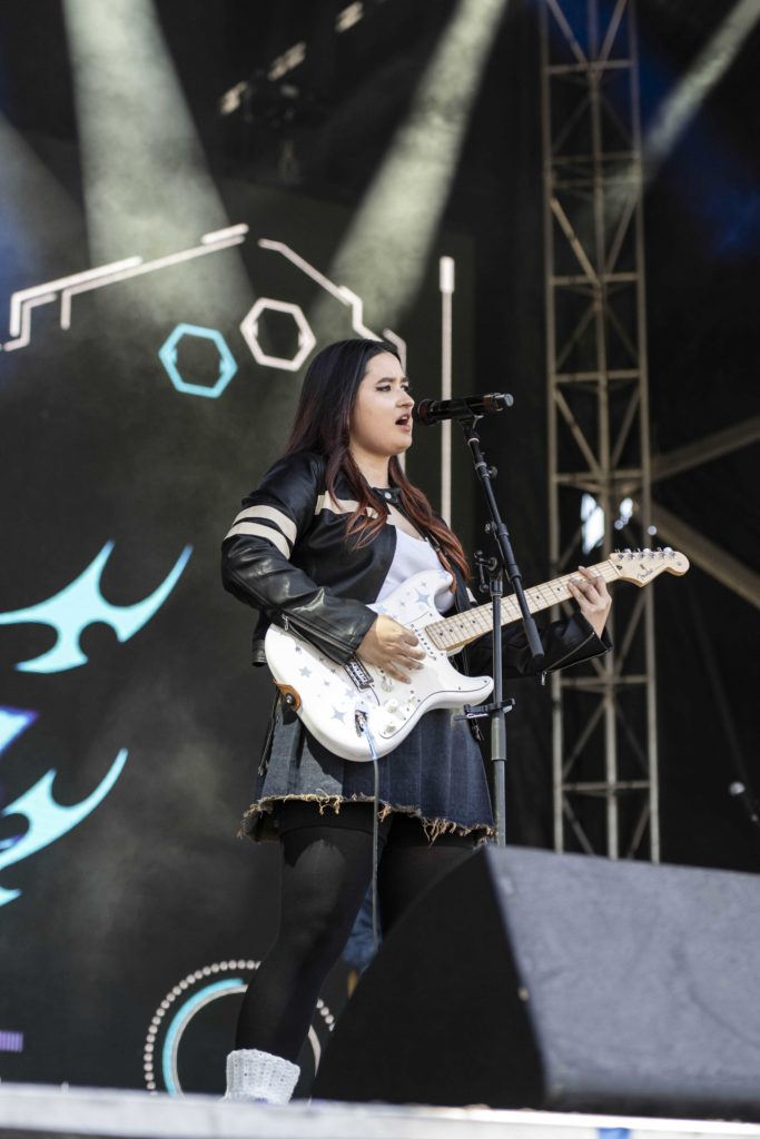 Poetri stands strumming her electric guitar in front of blue and white onscreen visuals. Poetri said her music has taken on more of a rock characteristic as she's grown. (Megan Cai/Daily Bruin senior staff)