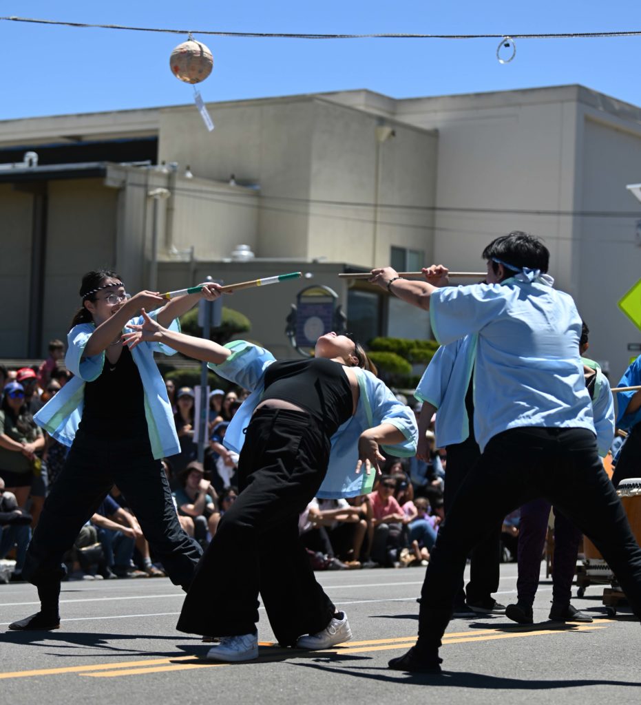 Ping He (left) and Taylor Lee (right) take mirrored stances as Michelle Duong (center) leans backward during a performance under the San Jose sun. Rising fourth-year biology student Duong said the drumming ensemble's musical repository includes songs that are unique to the club and pieces composed by its members. (Courtesy of Riley Stokes)