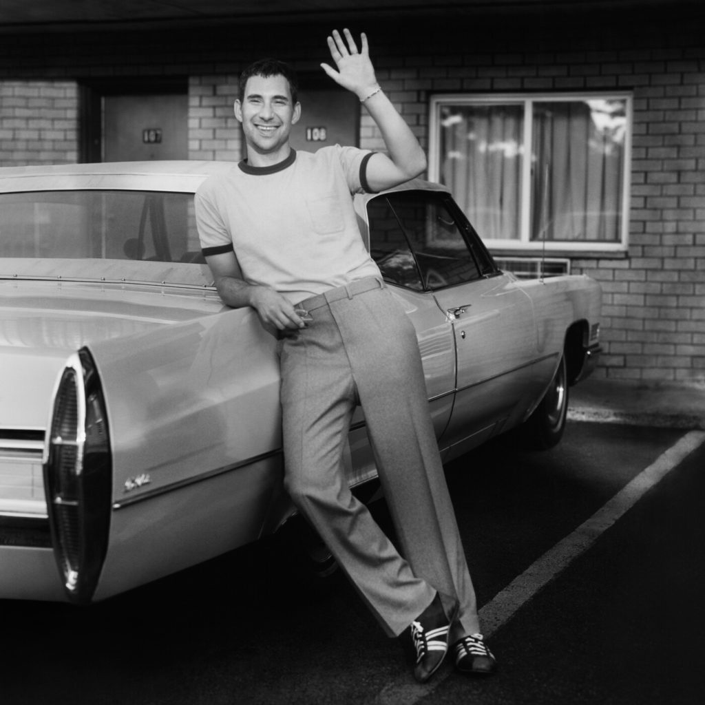 In the retro-style "bleachers" album cover, a man in a simple tee and slacks leans against a car and waves. The band&squot;s self-titled album contains 14 new tracks and will be released on March 8. (Courtesy of Dirty Hit Records)