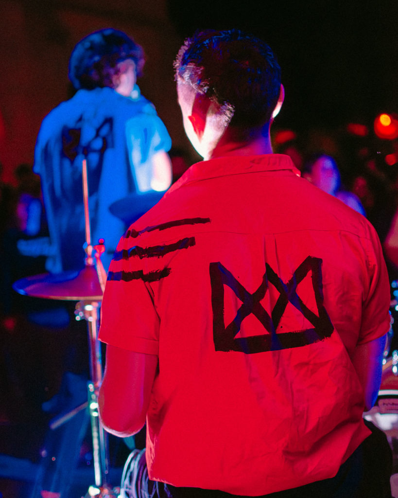 Seated in front of a drum kit, Greyson Suchecki sports a red button-up with black streaks and a crown symbol. August Suchecki said the name Royal Fools is a play on the duality of musicians as individuals who are highly-regarded, yet expected to act in a comical manner for entertainment. (Courtesy of Royal Fools)