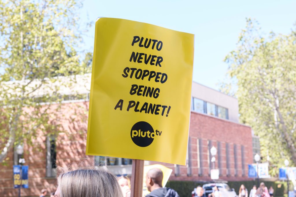 A yellow sign reads "Pluto never stopped being a planet!". Participants at the Monday rally said dwarf planets such as Pluto ought to be considered planets. (Leydi Cris Cobo Cordon/Daily Bruin senior staff)