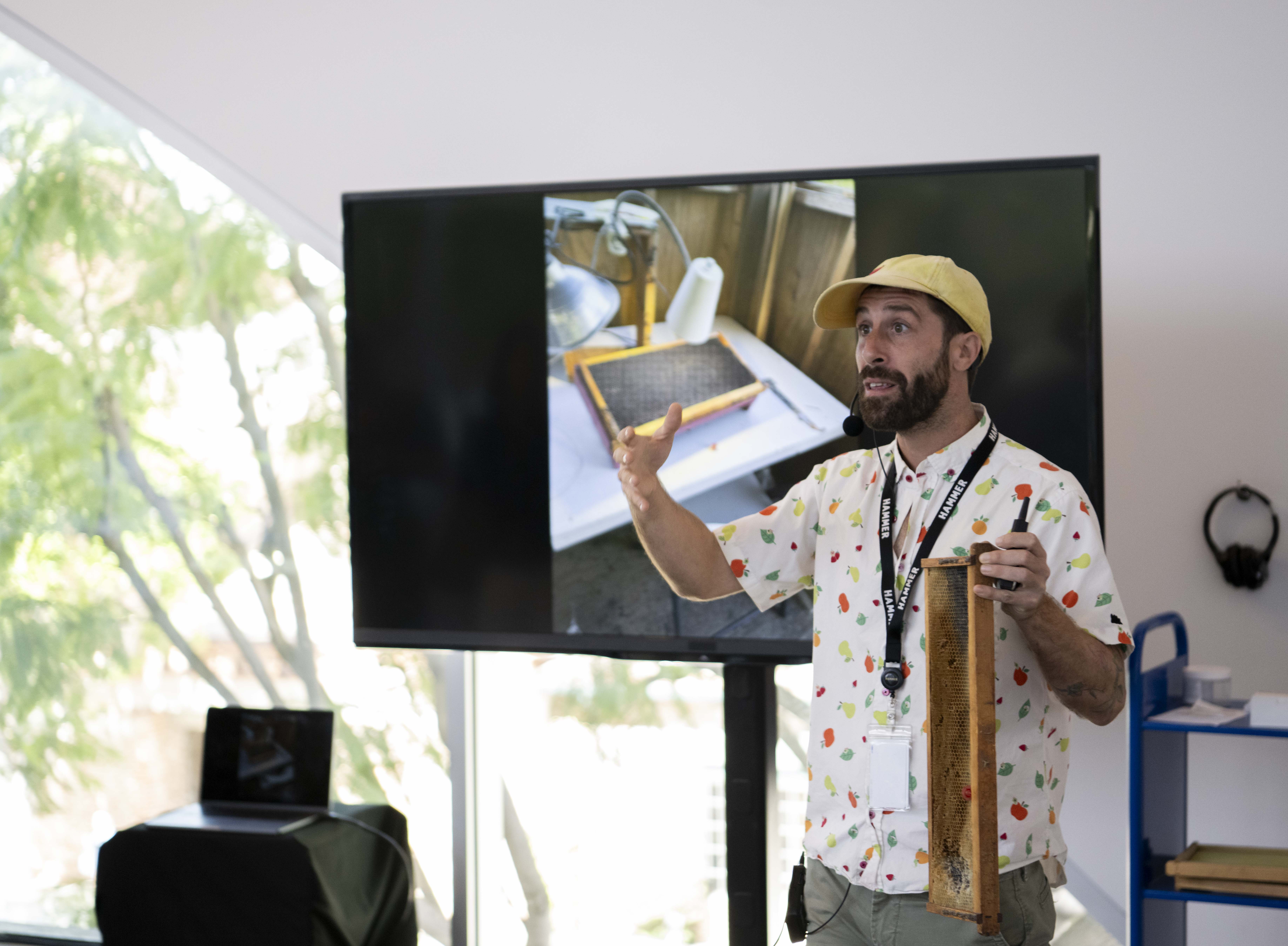 Pictured is Joe O'Brien in front of a screen and holding a comb honey frame. O'Brien's presentation was accompanied by the sculptures of fellow beekeeper, Garnett Puett. (Mia Tavares/Daily Bruin senior staff)