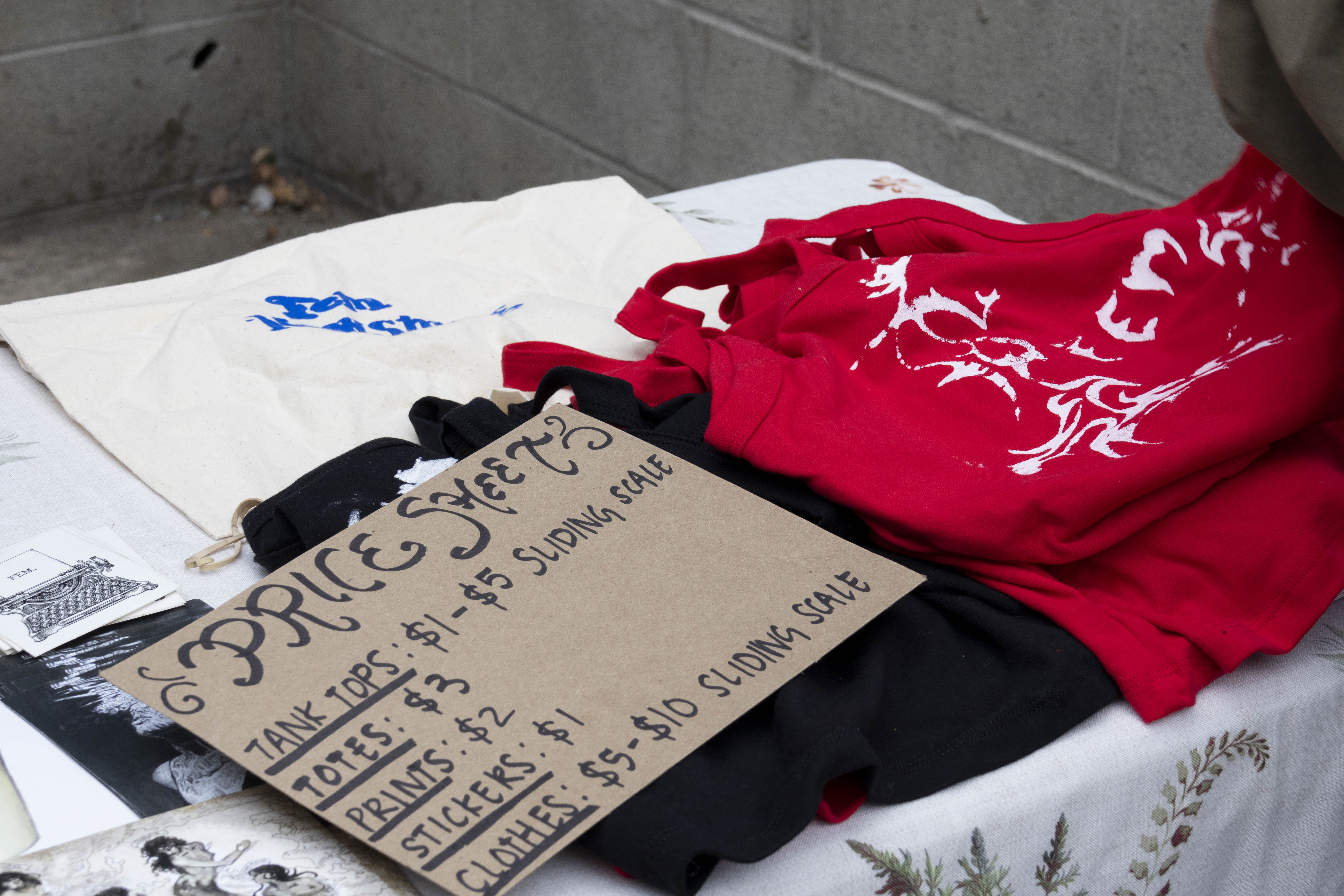 A sign detailing price range sits on top of merch from FEM Newsmagazine. Members of the newsmagazine brought merch and clothing to sell on a sliding scale for fire relief donations. (Selin Filiz/Daily Bruin)