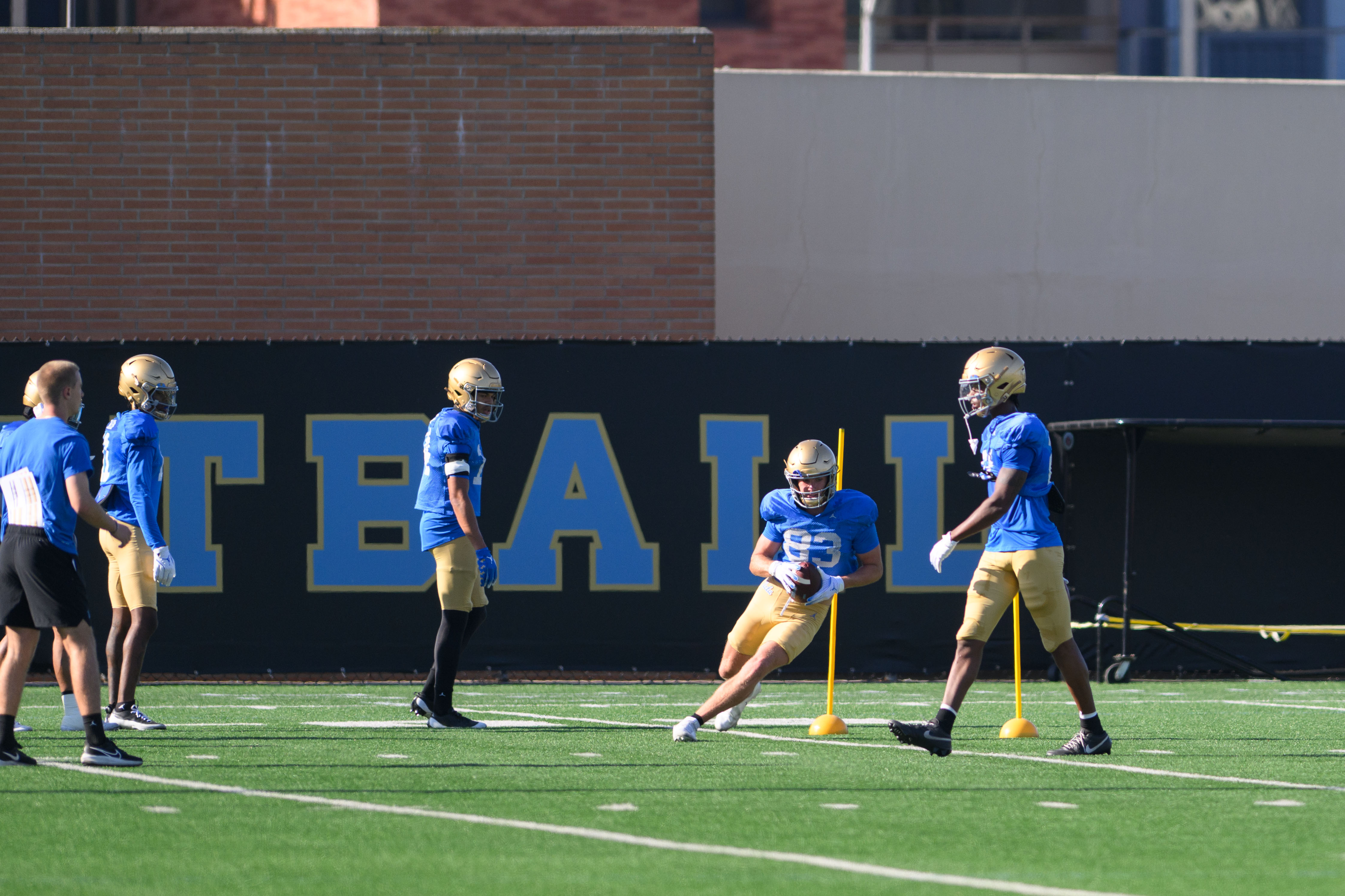 UCLA football's wide receivers go through position drills – specifically cut-and-catch drills to simulate sharp route breaks around yellow poles. (Brianna Carlson/Daily Bruin staff)