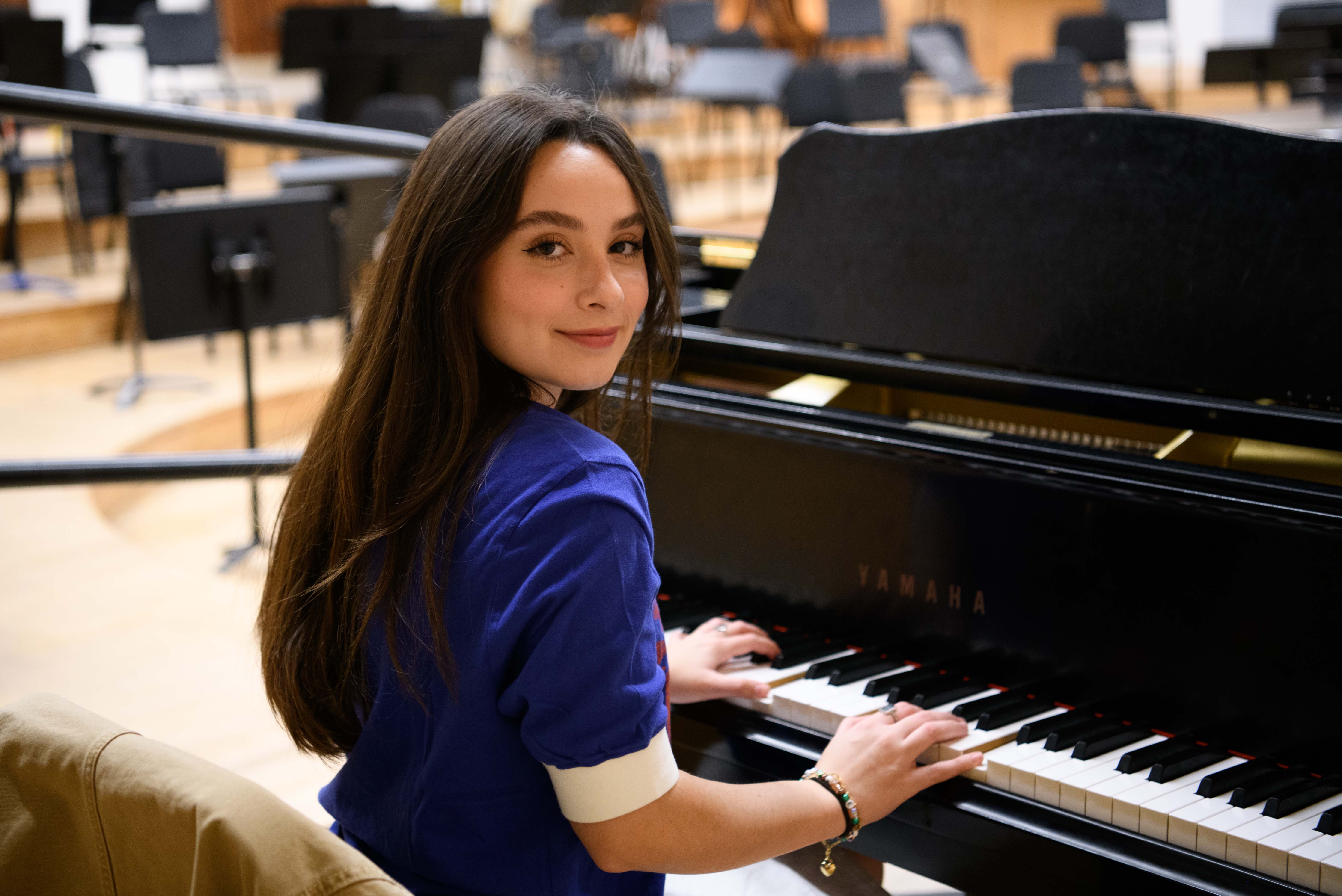 At a piano in a rehearsal room, Ava Ulloa sits and looks over her right shoulder while wearing a blue shirt. The student singer-songwriter said her musical influences include artists such as Sara Bareilles, Samara Joy and Lana Del Rey. (Amanda Velasco/Daily Bruin)