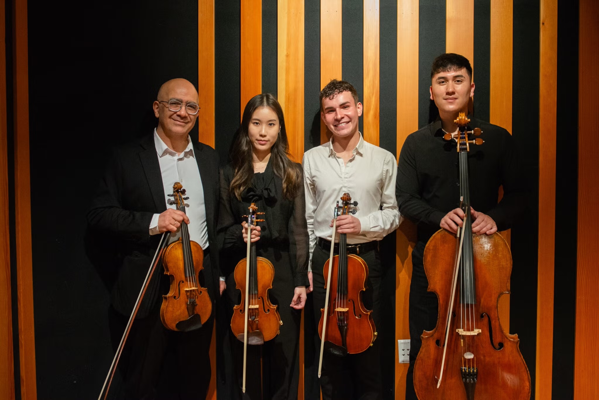 Members of the VEM Ensemble stand together for a photo against a black wall with vertical wood paneling. The ensemble is part of the Armenian Music Program at The UCLA Herb Alpert School of Music. (Courtesy of Melissa Bilal and The UCLA Herb Alpert School of Music)