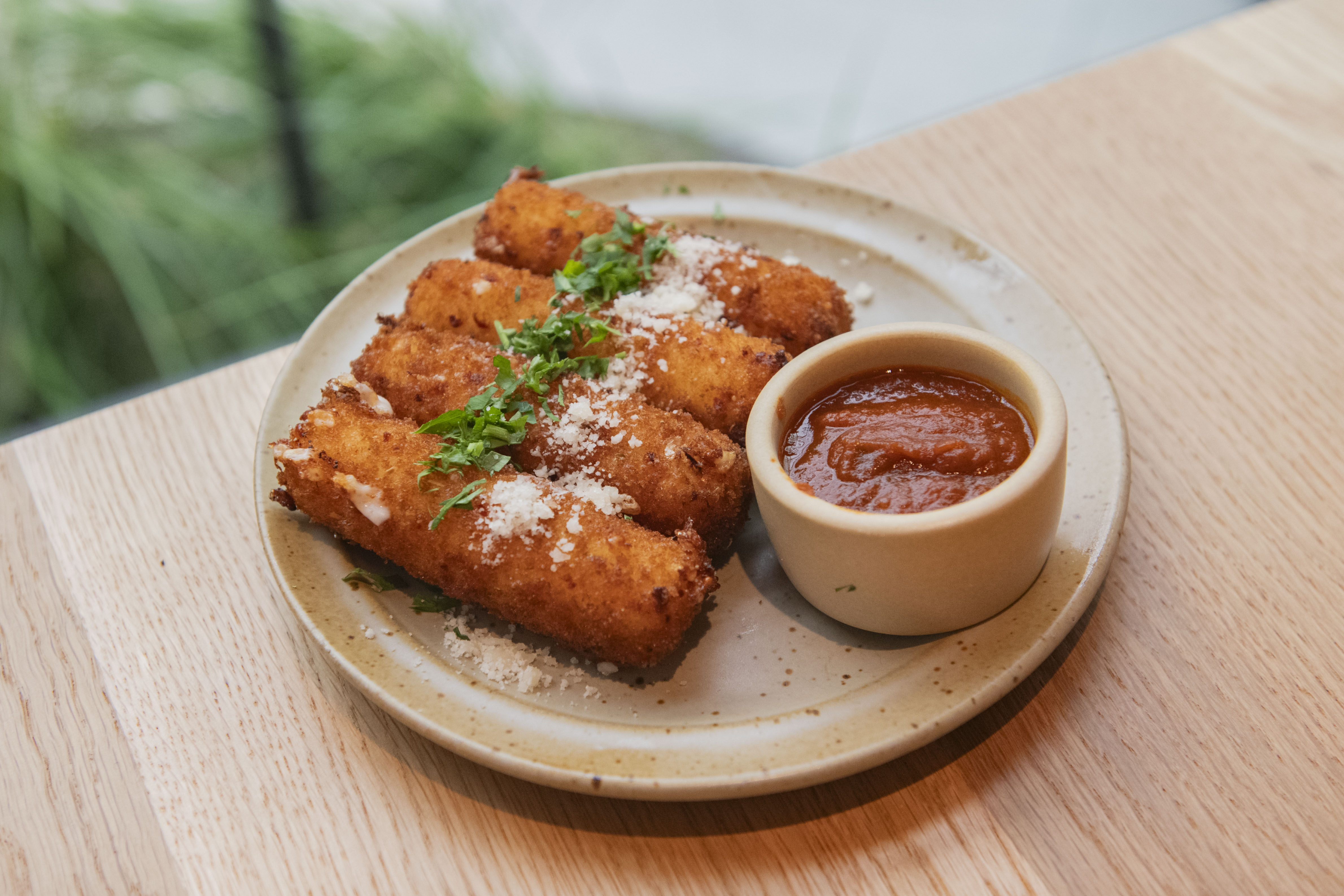 A small dish of four smoked mozzarella sticks are dusted with cheese and are plated next to a cup of marinara sauce while on a wooden table at Cosetta. The $16 appetizer is one of several "small plate" options offered at the Santa Monica eatery. (Karla Cardenas-Felipe/Daily Bruin staff)