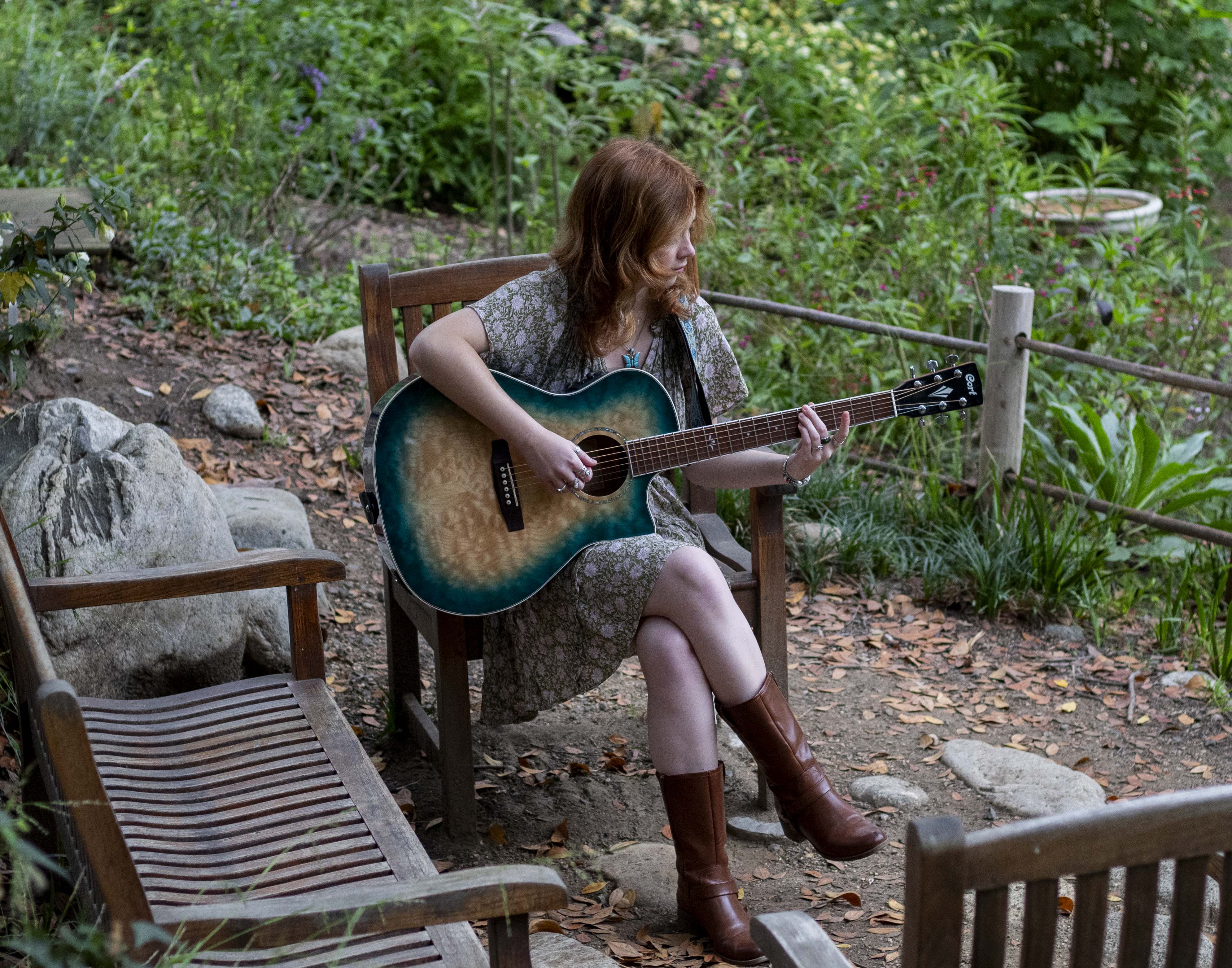 Ella Gibson sits in a wooden chair and plays her guitar while in a verdant garden. In preparation for her performance at Spring Sing, Gibson said she has worked on developing both her guitar instrumentation and her vocal technique. (Danielle Anz/Daily Bruin senior staff)
