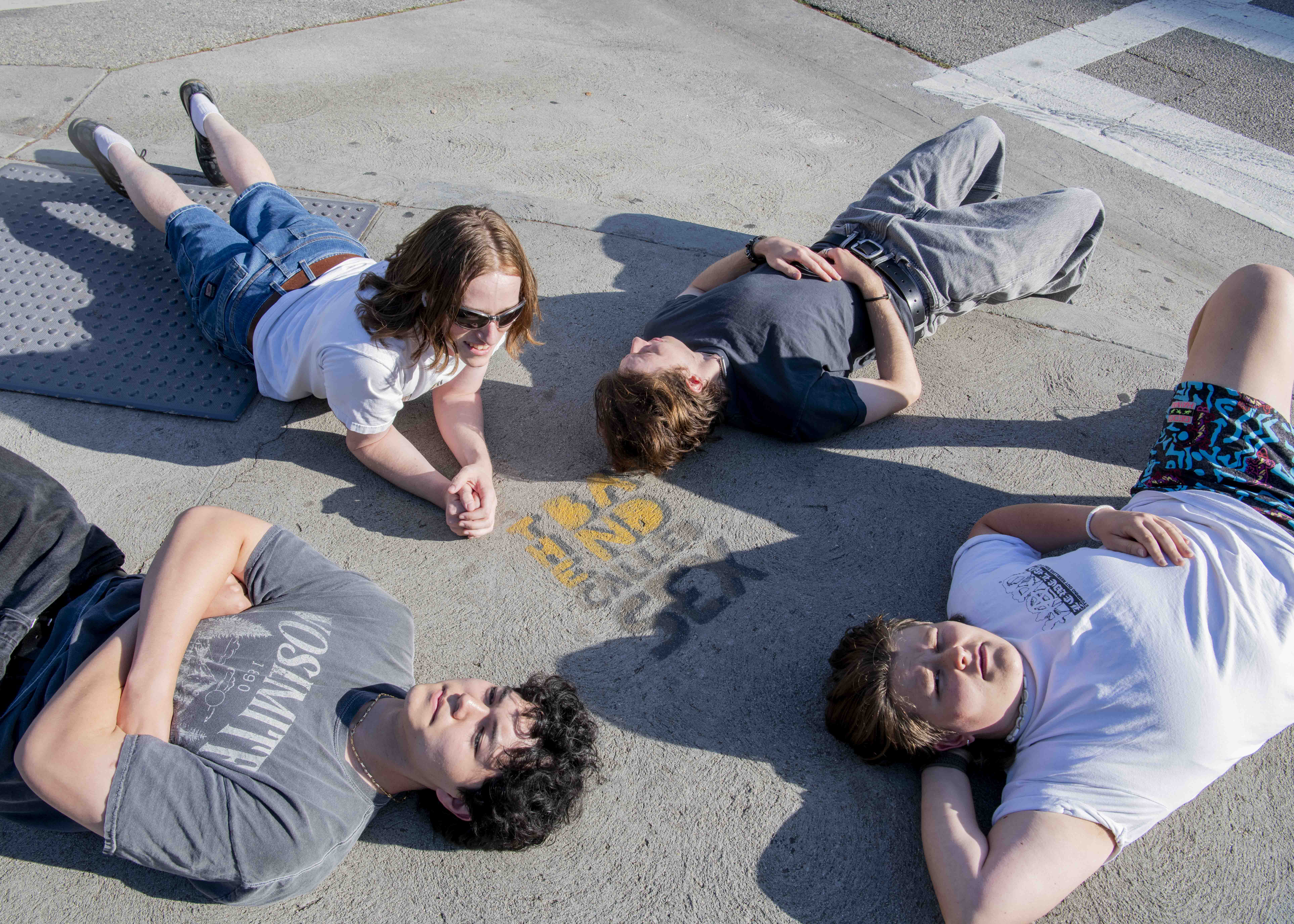 Four members of The Band Called Sex lie on the pavement next to a graffiti mark of the band's name. The group is currently in the process of working on an album. (Ruby Galbraith/Daily Bruin