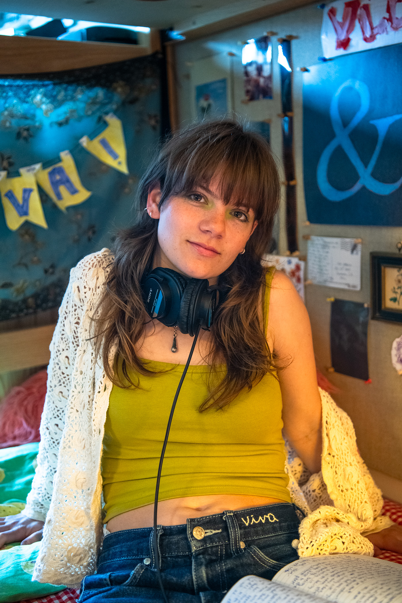 Viva Corless sits on a bed and looks toward the camera while wearing a set of headphones around her neck. She said she enjoys the ability to share stories and experiences in her songs. (Isabella Appell/Daily Bruin)