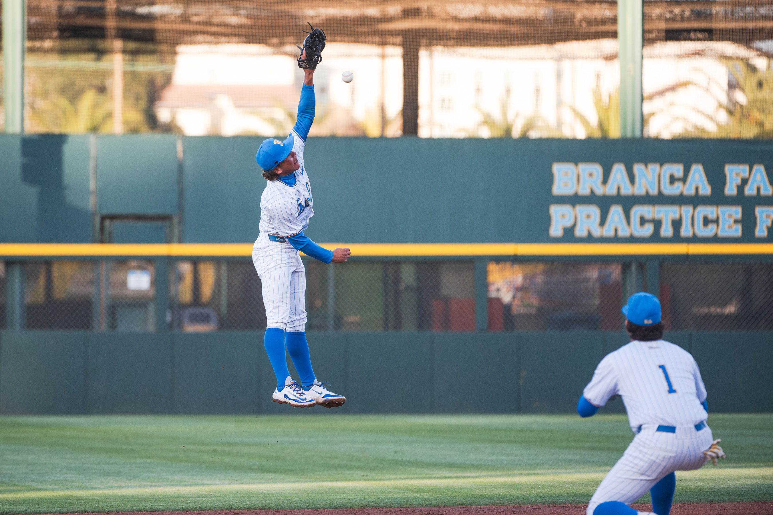 Sophomore second baseman Phoenix Call (left) makes a leaping snag on the infield while sophomore shortstop Roch Cholowsky (right) watches nearby. (Jeannie Kim/Daily Bruin senior staff)