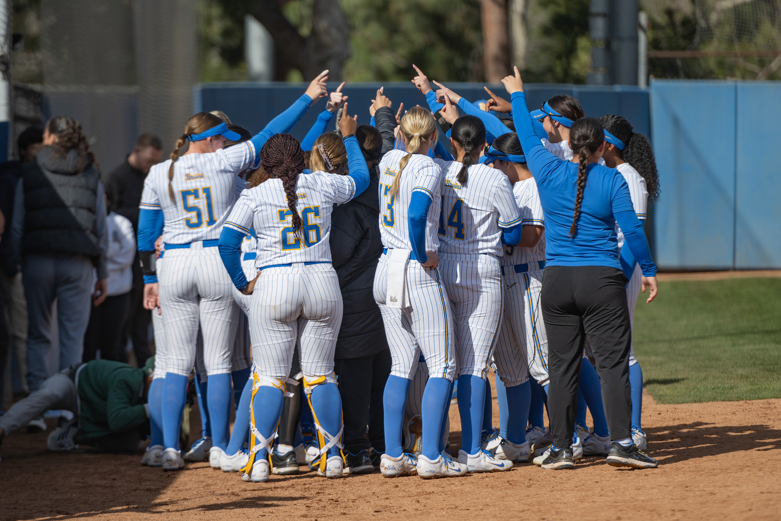 UCLA softball huddles together near the outfield grass. (Edward Ho/Daily Bruin)