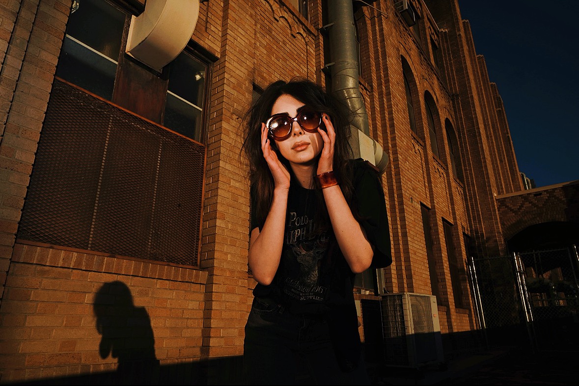 Leaning forward with her hands framing her face, the singer poses for a photo on the side of a building, casting a shadow on the wall. Although involved with music since middle school, Marcy said she didn't begin considering a music career until later in life, when she discovered her passion for the creative process. (Courtesy of August Suchecki)