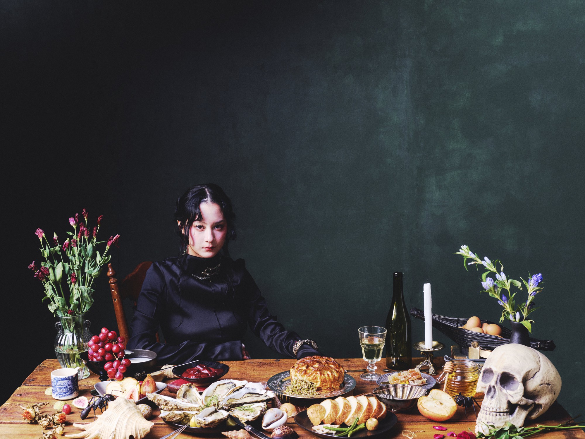Pictured is Japanese Breakfast's vocalist, Michelle Zauner, in front of a dark green background and sitting at a table with multiple dishes. The band will play at the Greek Theater along with opener Ginger Root. (Courtesy of Pak Bae and Grandstand Media)