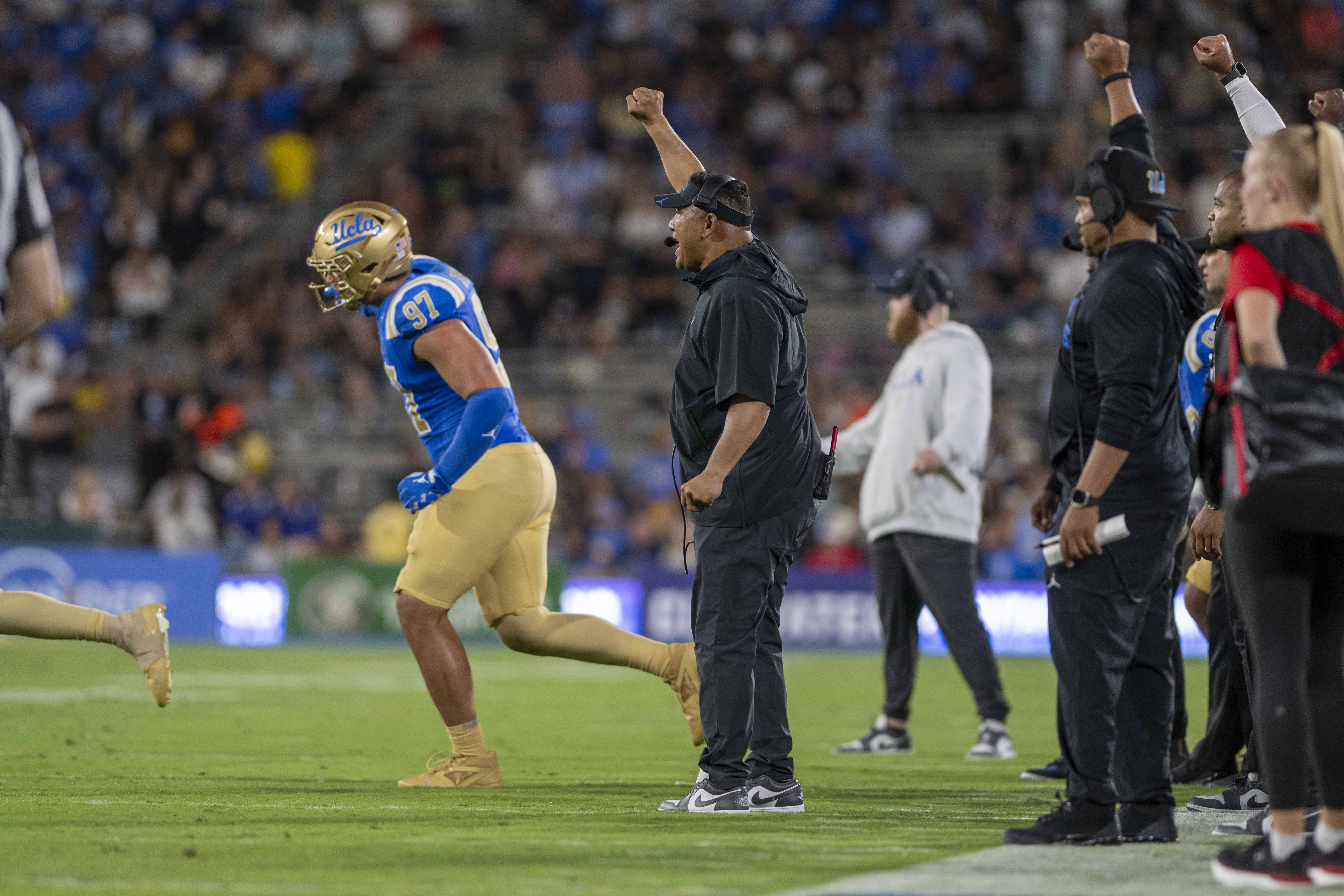 UCLA football defensive coordinator Ikaika Malloe raises his fist as he yells towards the field.