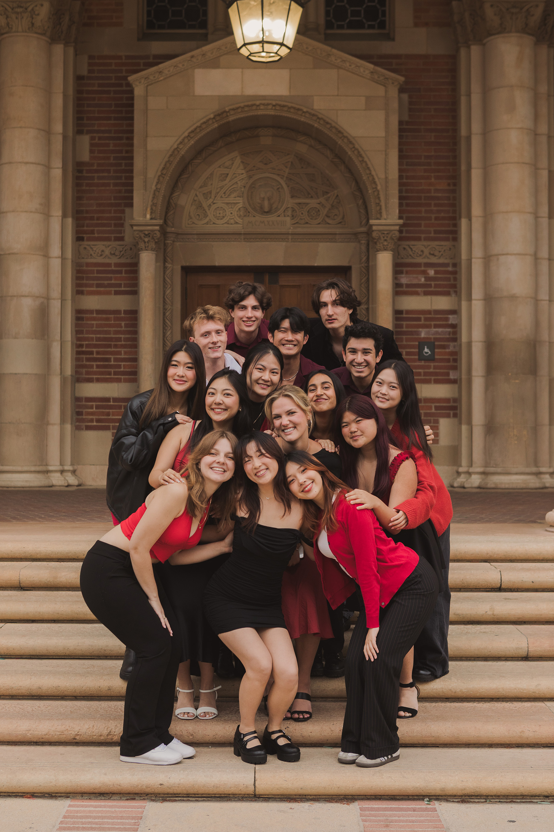 Group photo taken in Royce Hall's steps, with members wearing coordinated red and black attire. Diedrich said there is a community between all of the a cappella groups on campus, often participating in fun events together, such as Aca-prom. (Courtesy of Ava Diedrich and Pitch, Please!)