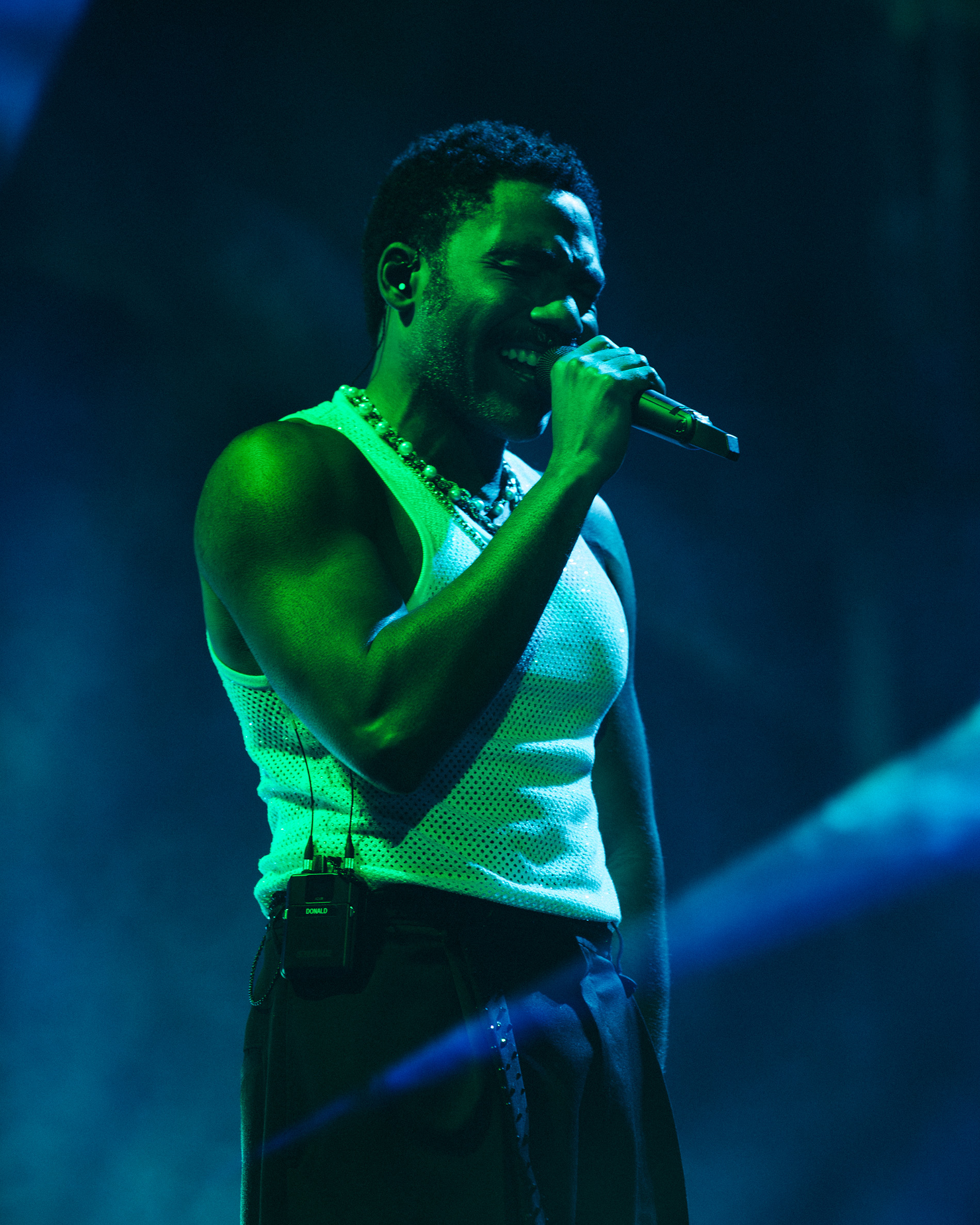 Childish Gambino is bathed in a green light while wearing black trousers and a white mesh tank top. The actor and singer performed snippets of all-time fan favorites in hopes of taking advantage of the hour-long set. (Courtesy of Hayden Stills, AEG Presents IT)