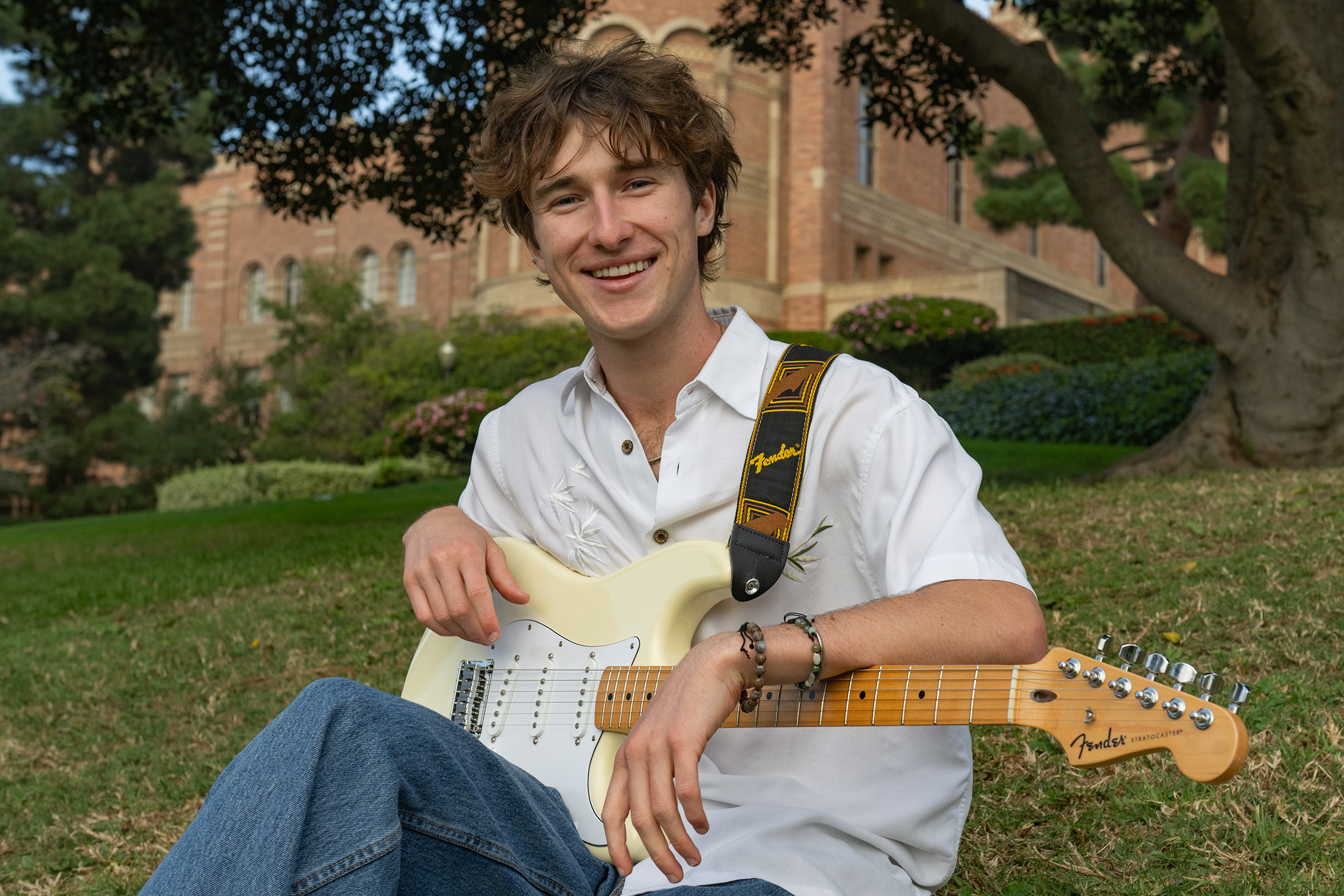 Wright sits in a green area wearing a white button-up and blue jeans. The artist said one of his favorite elements of making music is performing live, which he hopes evokes the same sense of spiritual inspiration he often experiences when attending live events. (Leydi Cris Cobo Cordon/Daily Bruin senior staff)