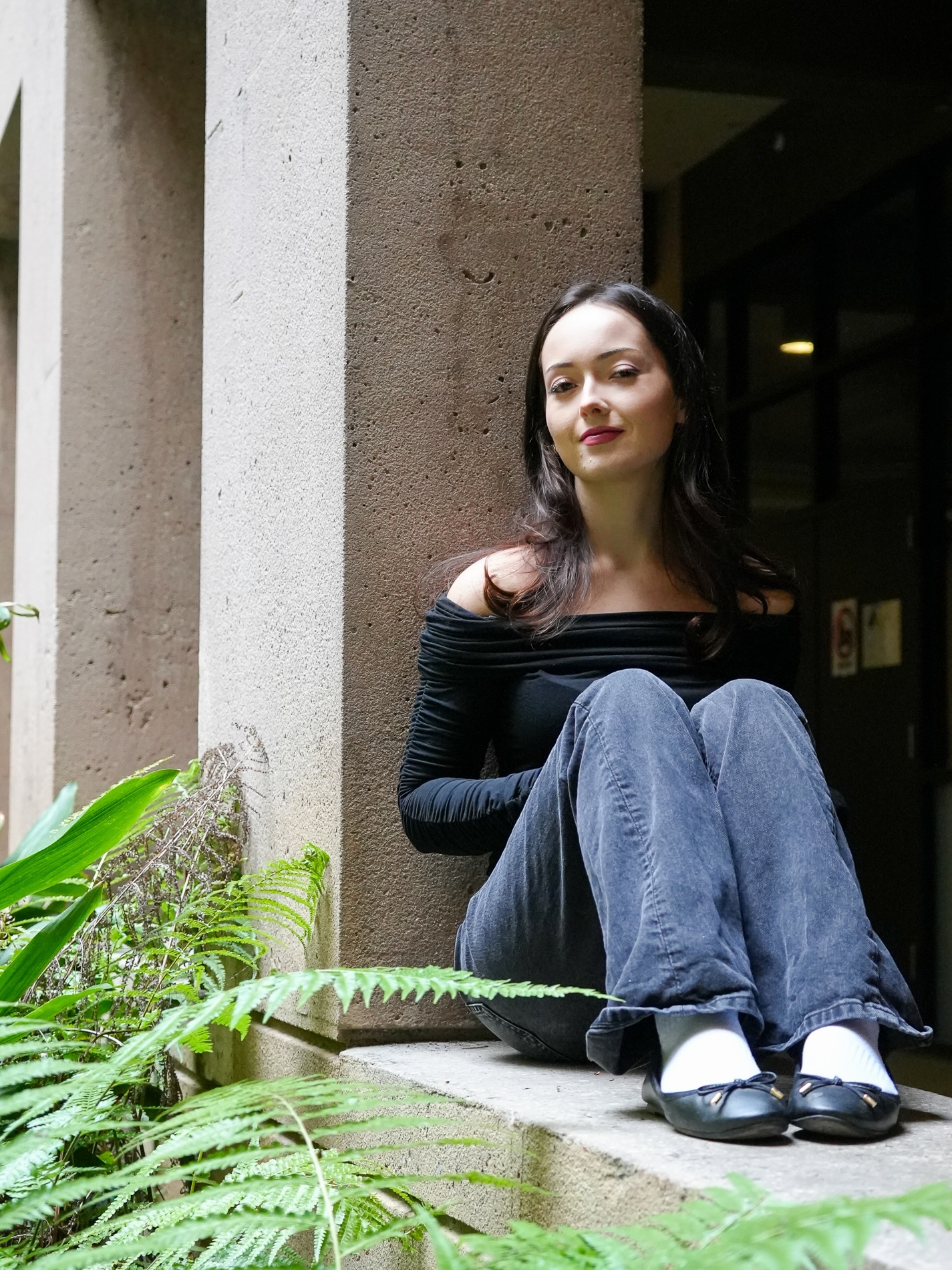 Sturges poses wearing blue jeans and a black off-the-shoulder shirt. While the student said she is still figuring out her sound, she has experimented with an R&B sound and leaned into electronic music since starting to DJ in her senior year of high school. (Makenna Kramer/Daily Bruin)