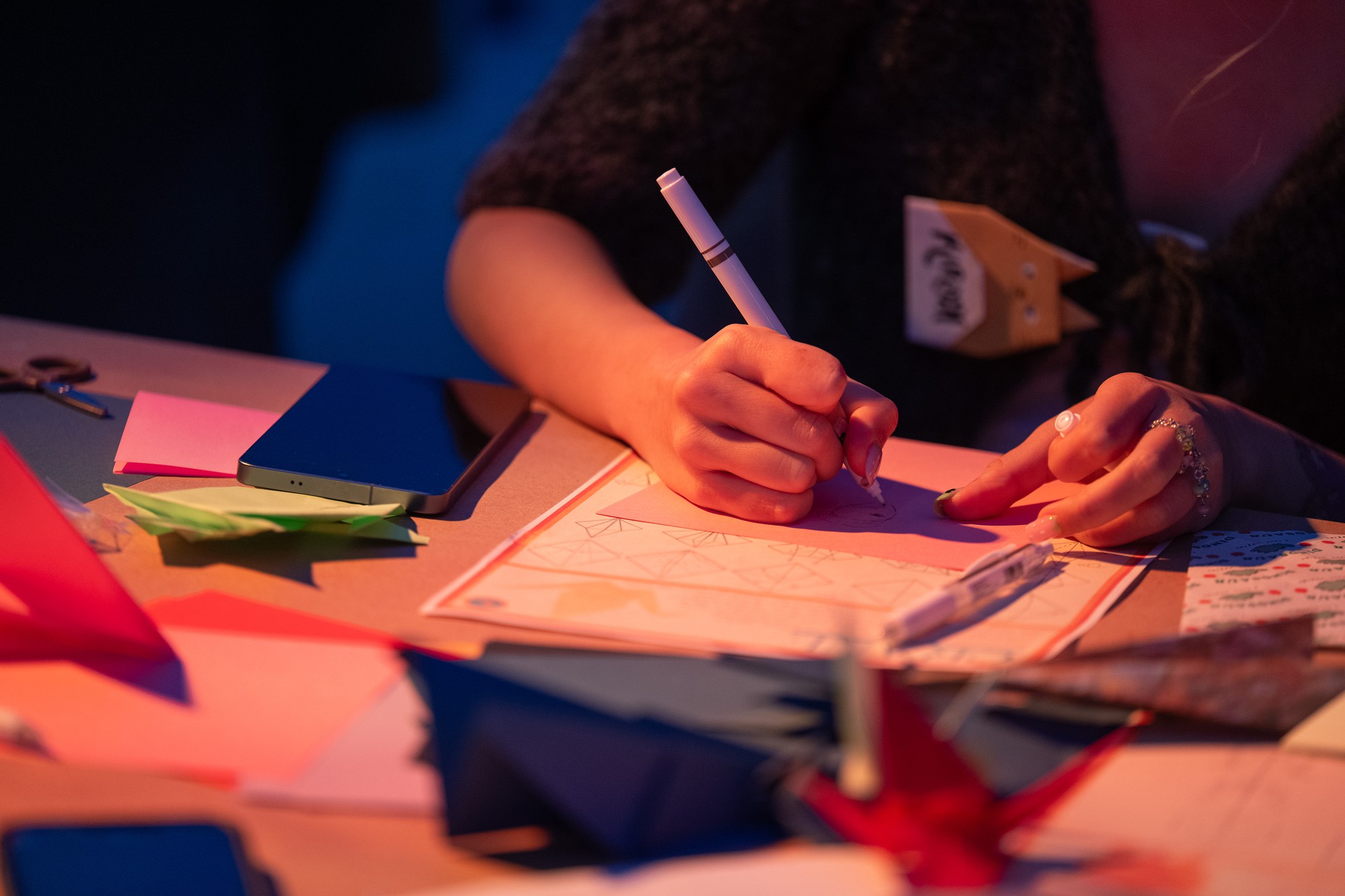 Shown are two hands drawing on a piece of paper with origami figures scattered across the table. The night's activities featured both physical art and performance readings, as well as music by DJ Hourglass and Brian Henry. (Selin Filiz/Assistant Photo editor)