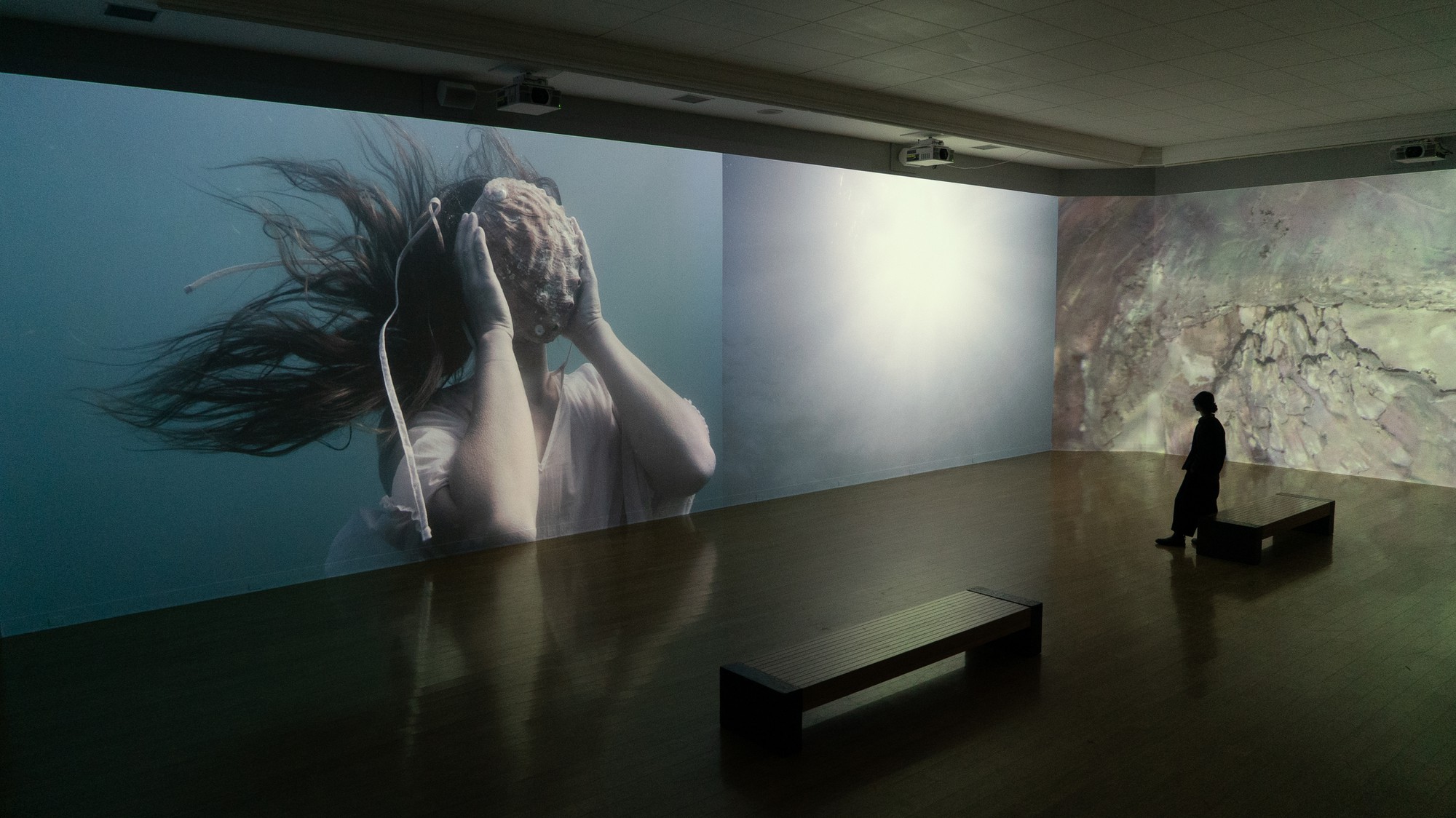 "The Sea Around Us" installation shows a video of a woman covering her face with an abalone shell. The installation, which is divided across six channels, depicts the consequences of poisonous waste dumping off the Southern California coast. (Courtesy of Rebeca Méndez)