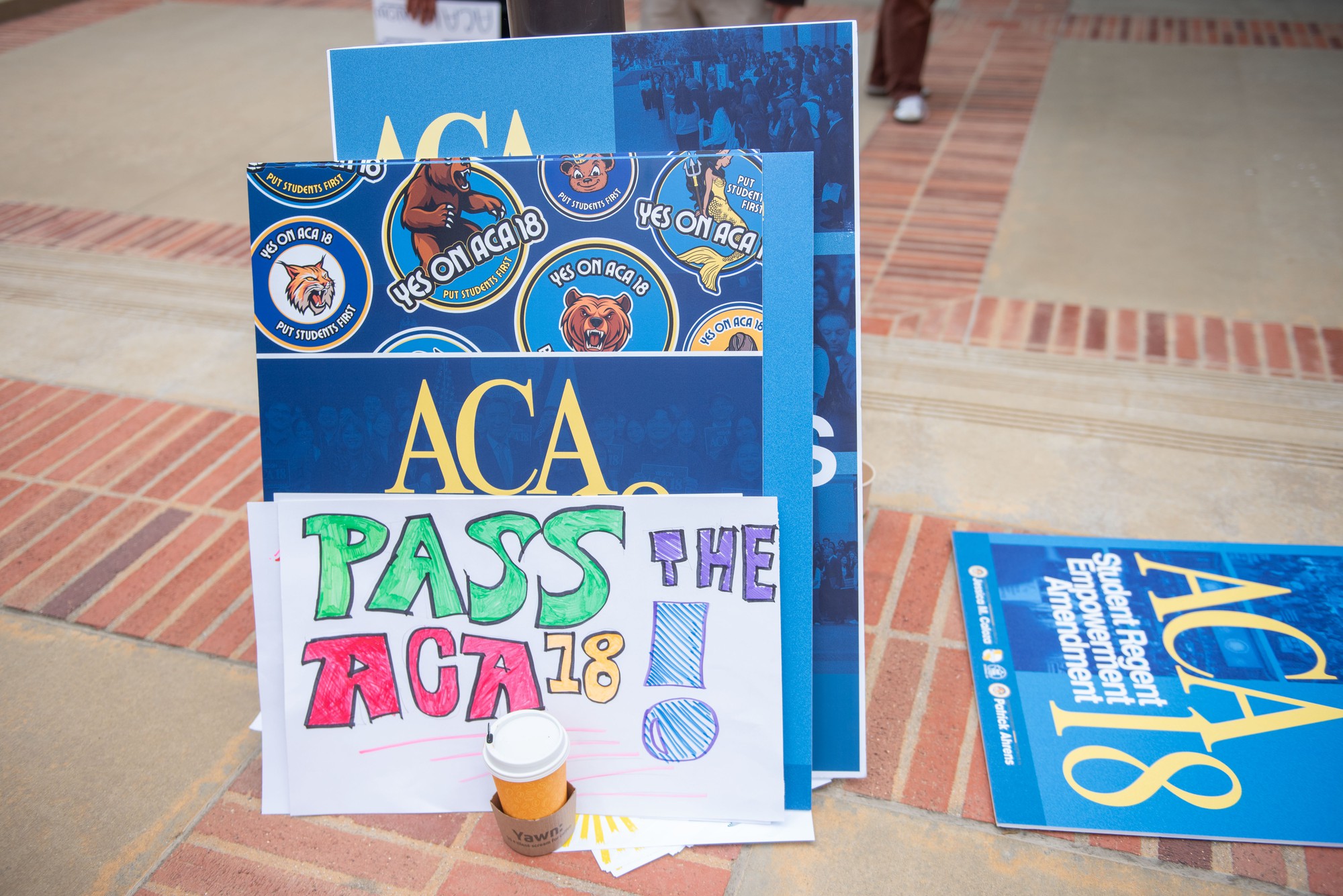 Posters in support of Assembly Constitutional Amendment 18, which would require the UC Board of Regents to appoint one undergraduate student and one graduate student to serve two-year terms on the board, lean against a lamppost. (Karla Cardenas-Felipe/Daily Bruin staff)