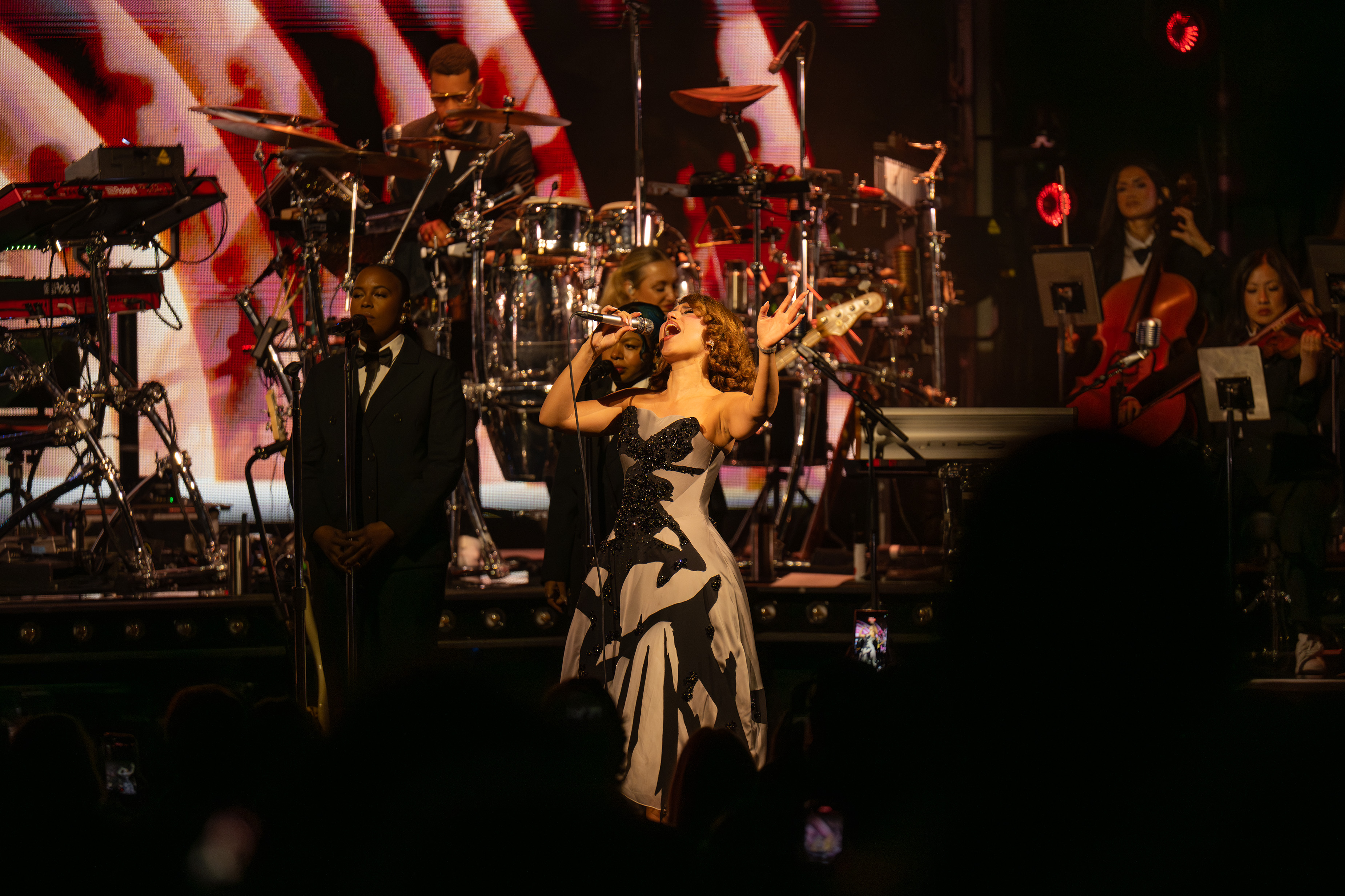 RAYE wears a long strappless dress as she leans back, belting out the notes of one of her songs. The show was divided into multiple acts, starting with a jazz club segment, going to a symphonic set and for the finale, a rave. (Bettina Wu/Daily Bruin senior staff)