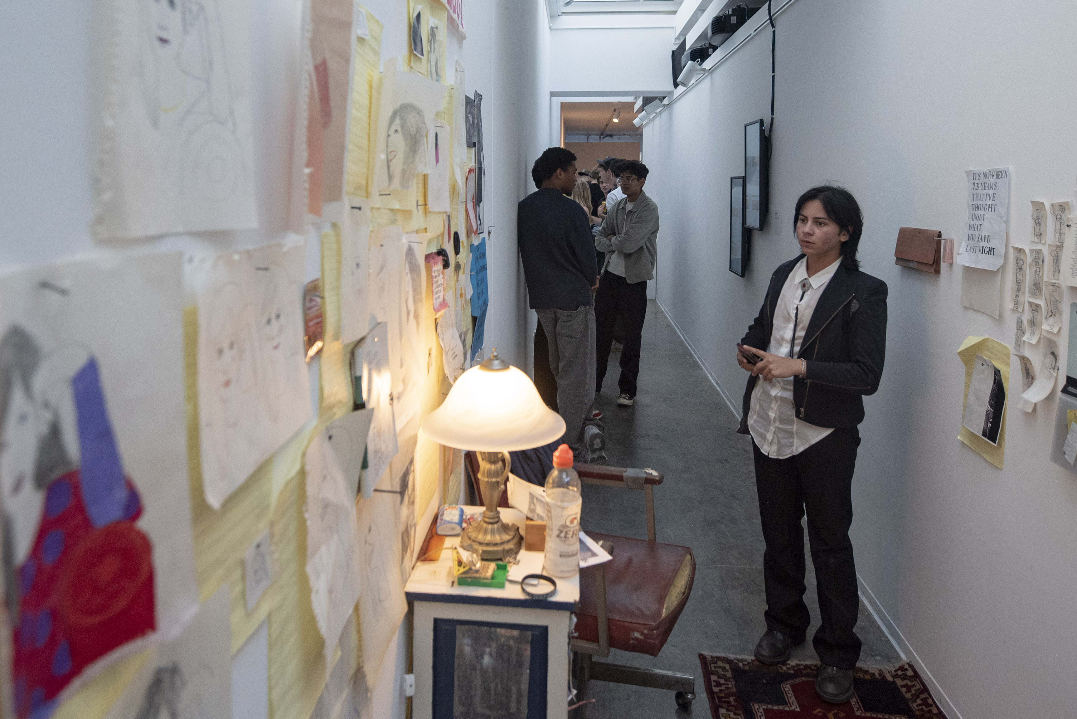 A student stands in a hallway looking at various papers and drawings hung on a wall. Fruition was on display until June 13th. (William Gauvin/Daily Bruin staff)