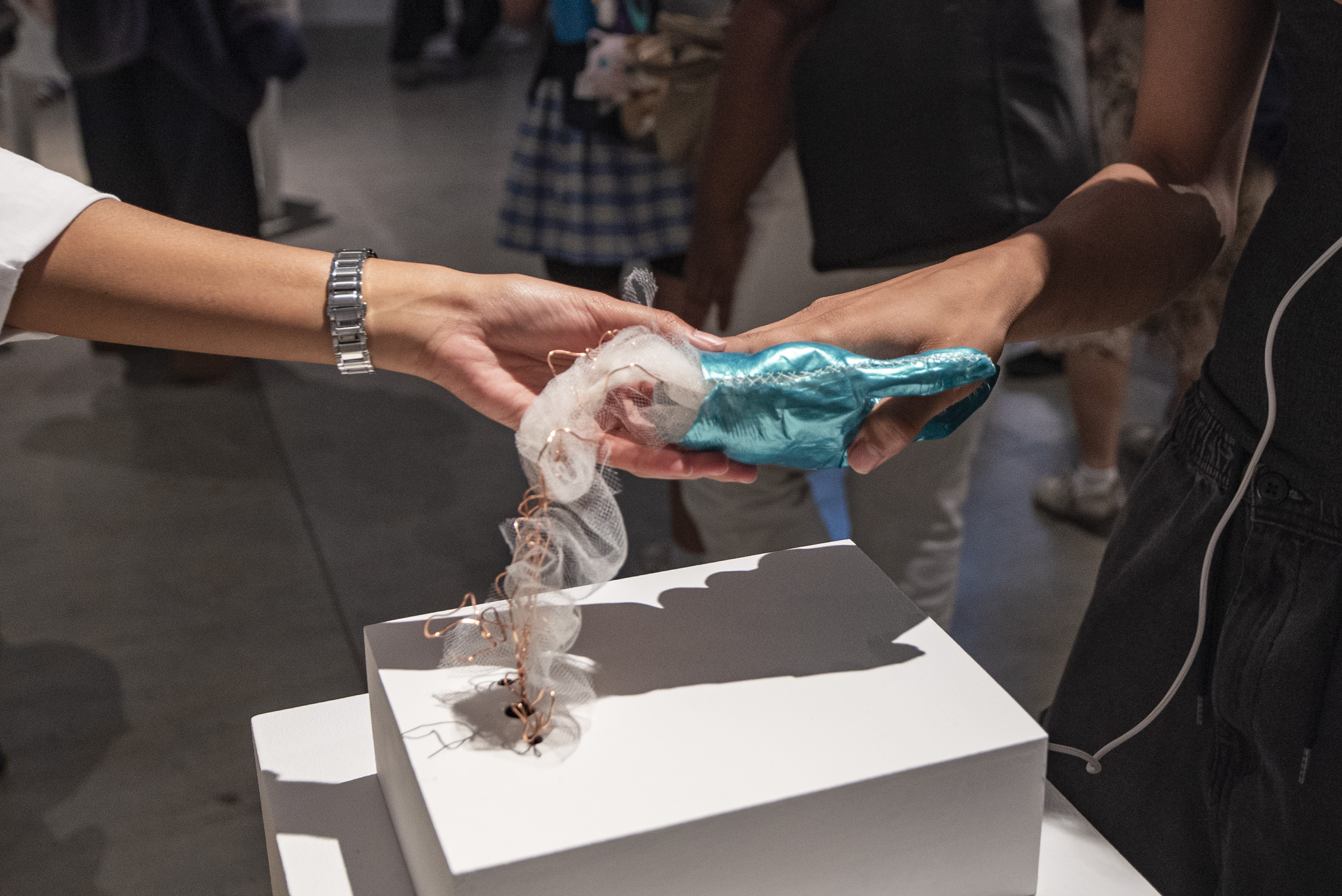 Two students interact with one of the art installations at Fruition. The installation involves a shiny blue gloved hand held up by copper wire. (William Gauvin/Daily Bruin staff)