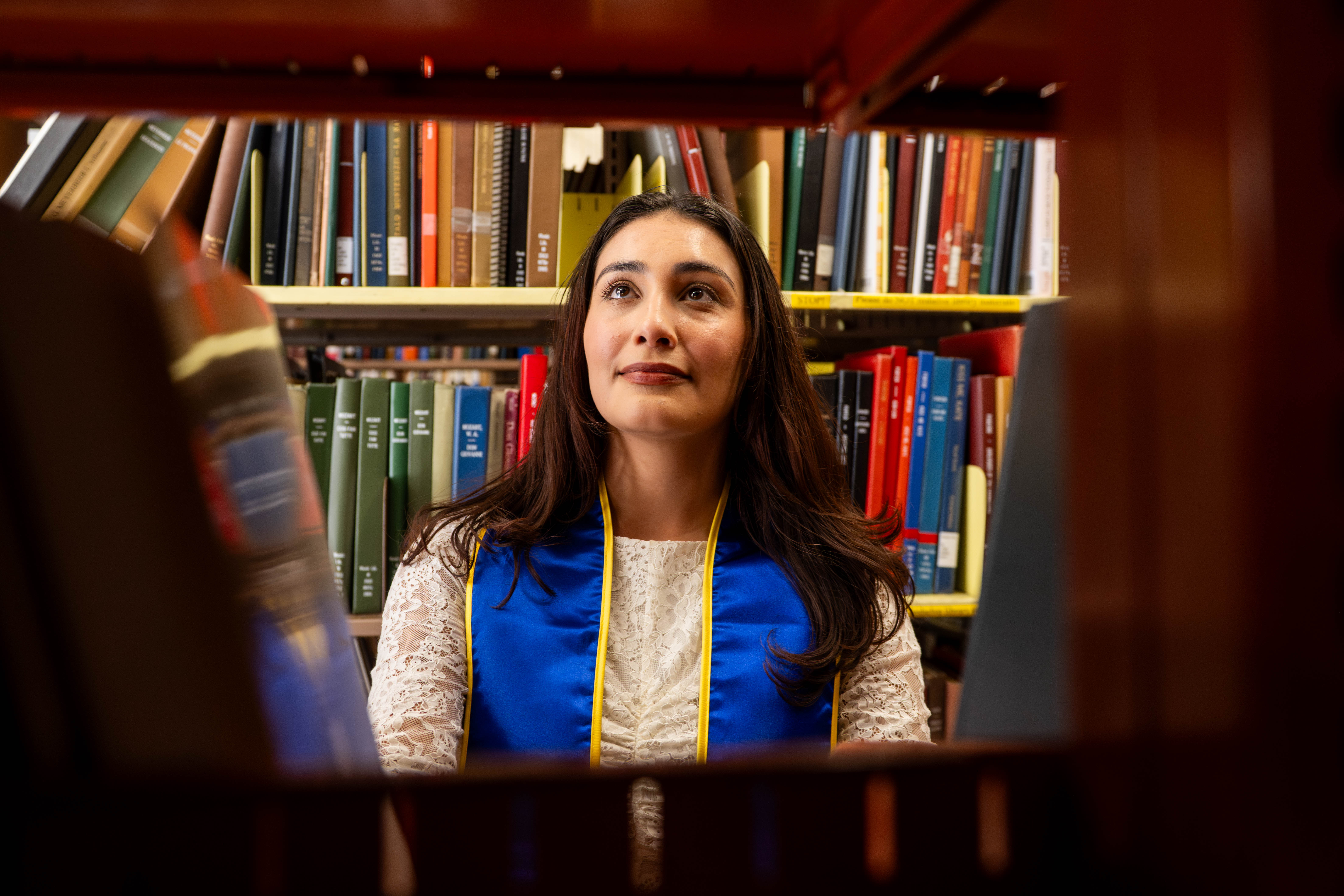 Robles' face is framed between books on a shelf. After graduation, Robles said she sees herself working at either an agency, a concert venue or as a concert promoter. (Andrew Ramiro Diaz/Photo editor)