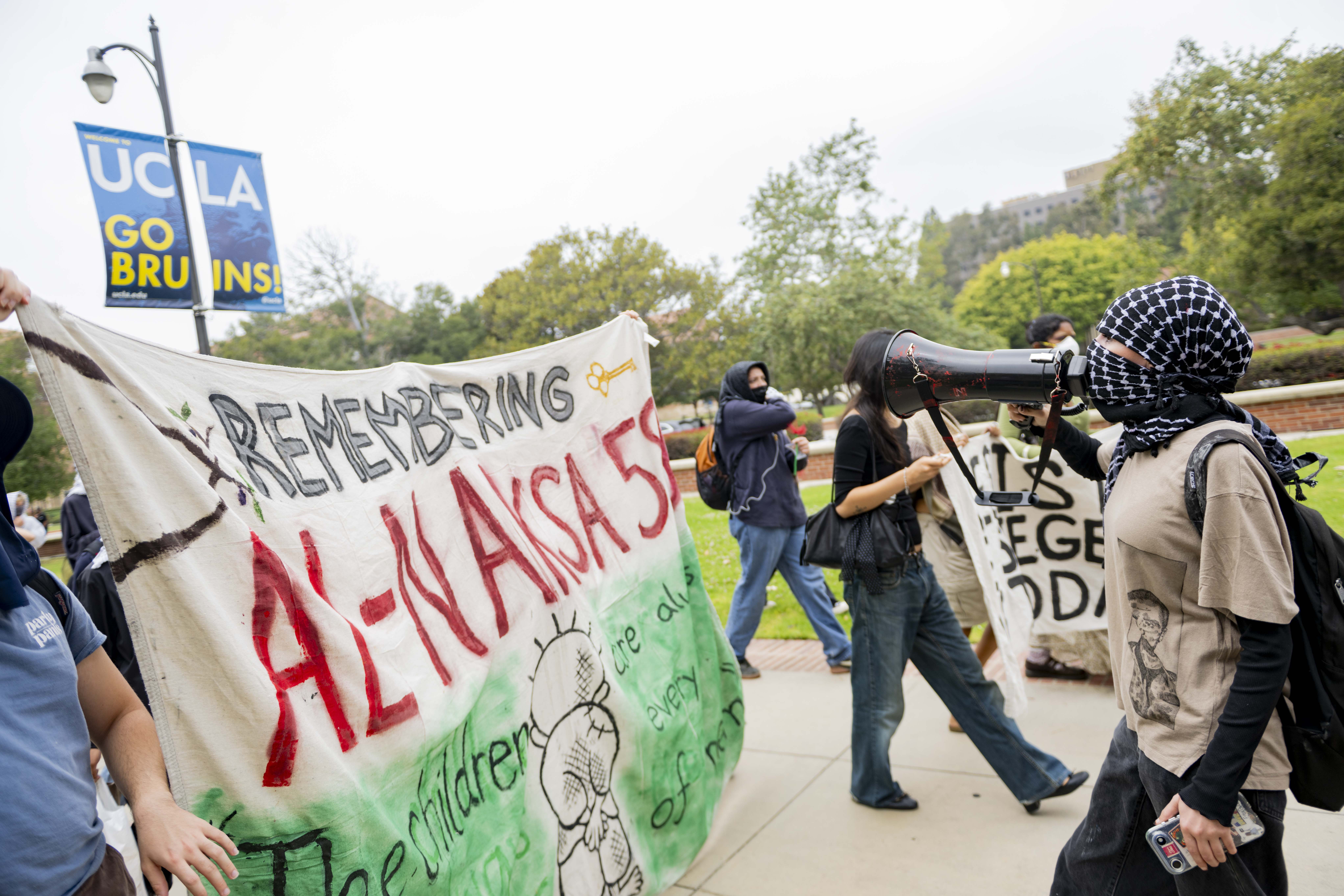 Protesters hold a banner as they walk through campus. About 35 people marched to demand UCLA divest from companies associated with the Israeli military, end on-campus policing and drop conduct cases against student demonstrators. (Andrew Ramiro Diaz/Photo editor)