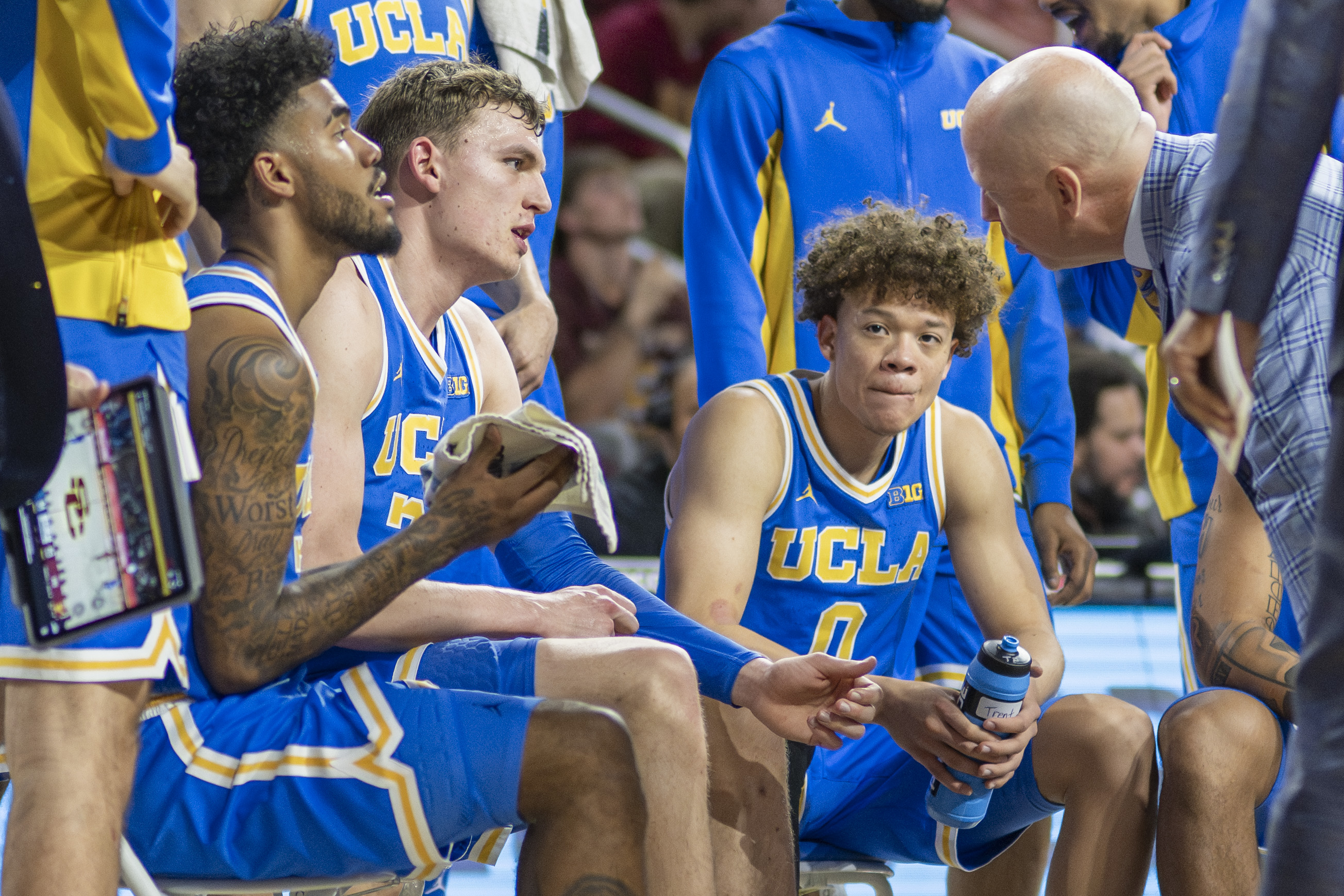 Left to right: Guard Donovan Dent, Bilodeau and rising junior guard Trent Perry sit in a semicircle around coach Mick Cronin during a timeout. Bilodeau is the only Bruin in the 2026 NBA Draft, with Dent retiring from professional basketball after graduating with Bilodeau. (Andrew Ramiro Diaz/Photo editor)