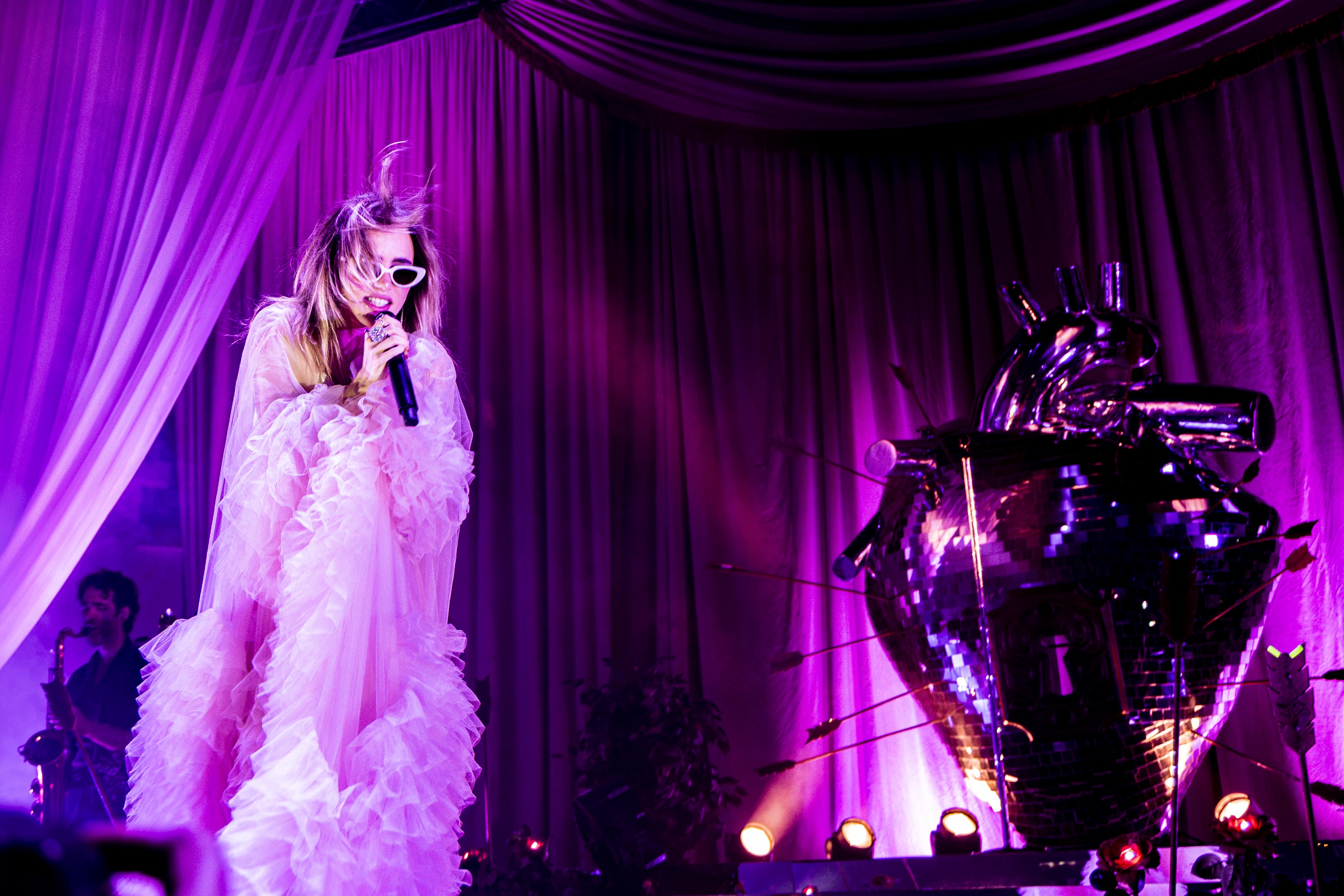 Waterhouse stands on stage looking down at the crowd. Framed with pink chiffon curtains and punctured with arrows, the stage held a mirror-tiled anatomical heart at the center. (Chenui Zhang/Daily Bruin staff)