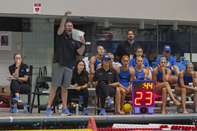 Former UCLA women’s water polo coach Adam Wright stands by the pool deck and points while holding a sheet to his mouth. Wright led the program to its first national championship since 2009 in 2024. (Daily Bruin file photo)