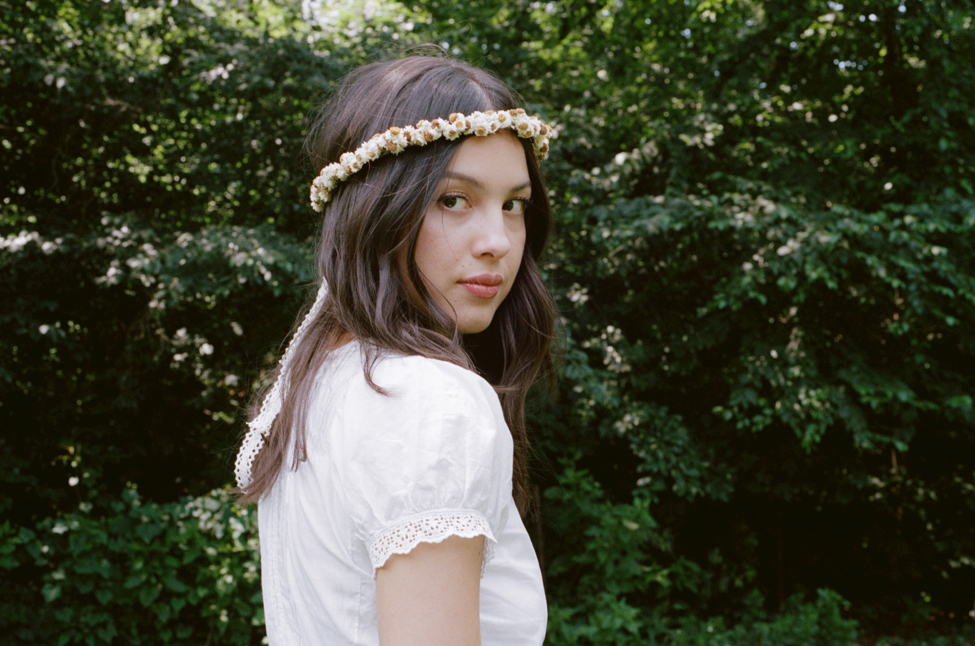 Olivia Rodrigo stands in front of greenery wearing a white top and flower crown. Daisy Chain Fields, a music festival founded by the singer, is taking place Saturday at Great Park in Irvine, featuring an all-women lineup to raise funds and awareness supporting women and girls. (Courtesy of Marissa Lomis)