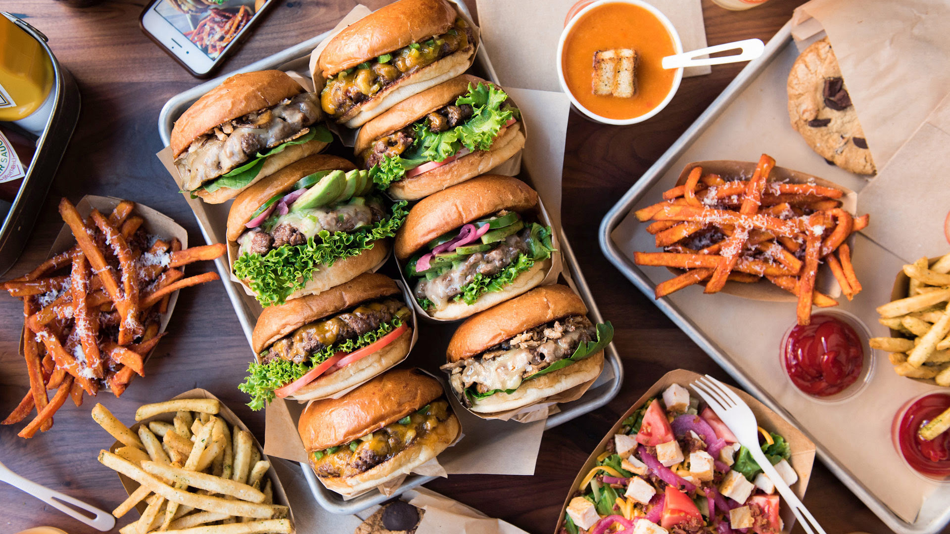 Burgers from The Melt are shown alongside several of the restaurant's sides, including classic and sweet potato fries. The restaurant's 931 Westwood Boulevard location will open this fall. (Courtesy of The Melt)